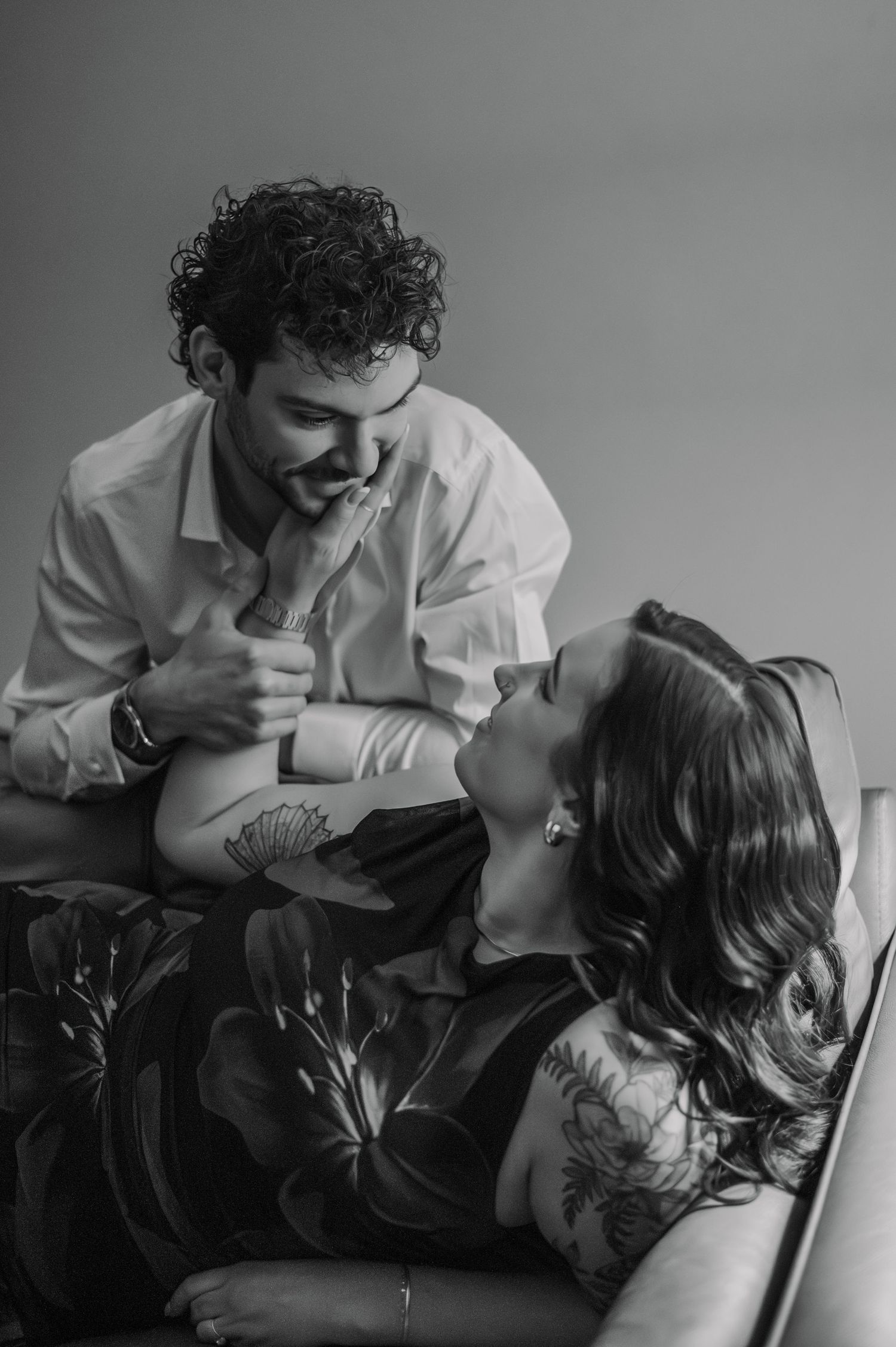 Black and white photo of a romantic couple, woman lying back gazing up at smiling man on a couch.