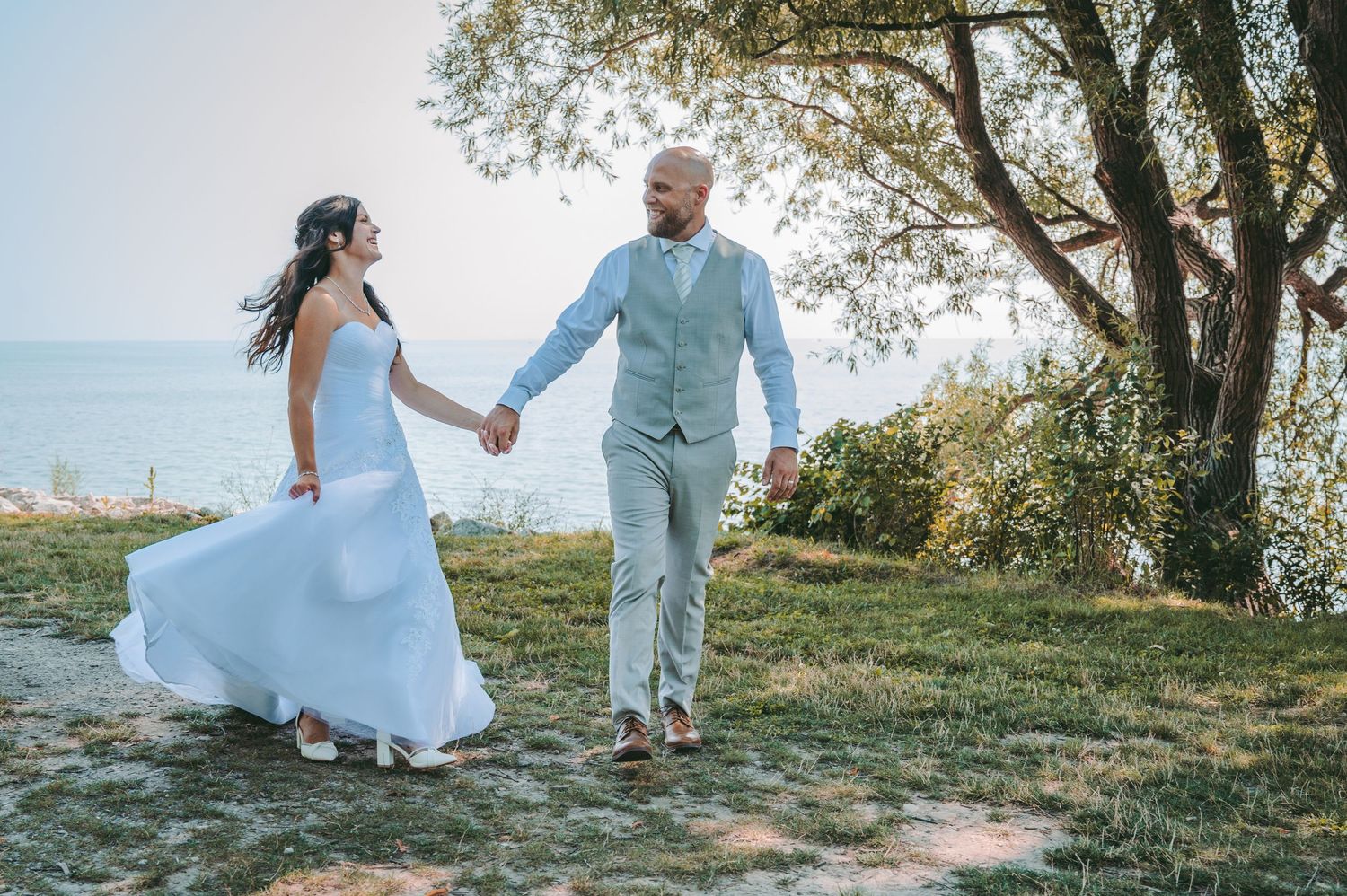 Bride and groom holding hands walking outdoors near ocean trees on their wedding day.