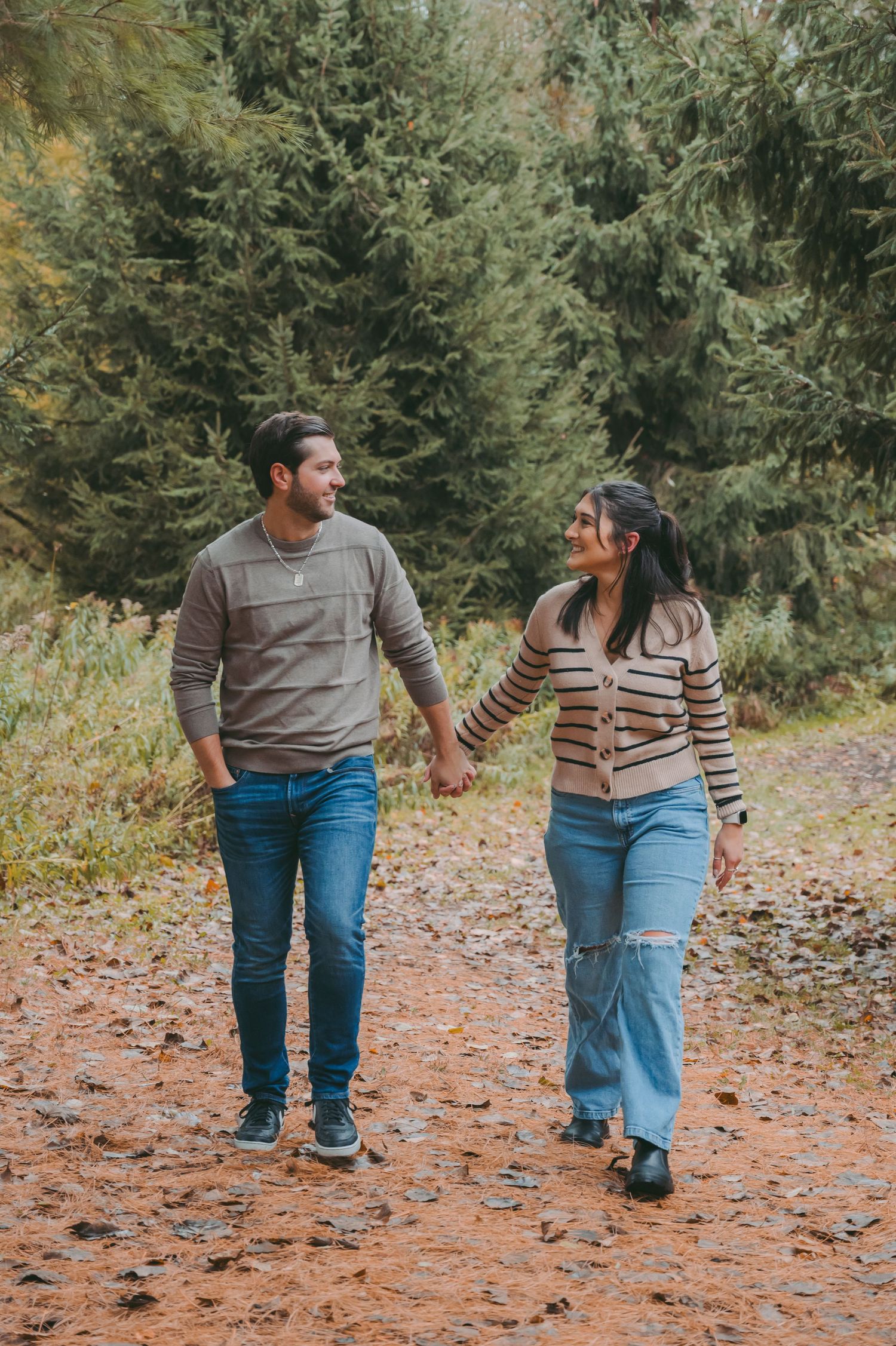 Couple walking hand in hand on a forest trail wearing coordinated casual outfits.
