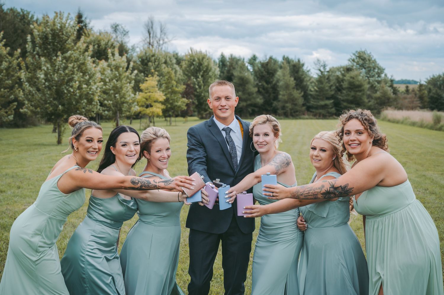 Bridal party in mint green dresses posing playfully with the groom outdoors.