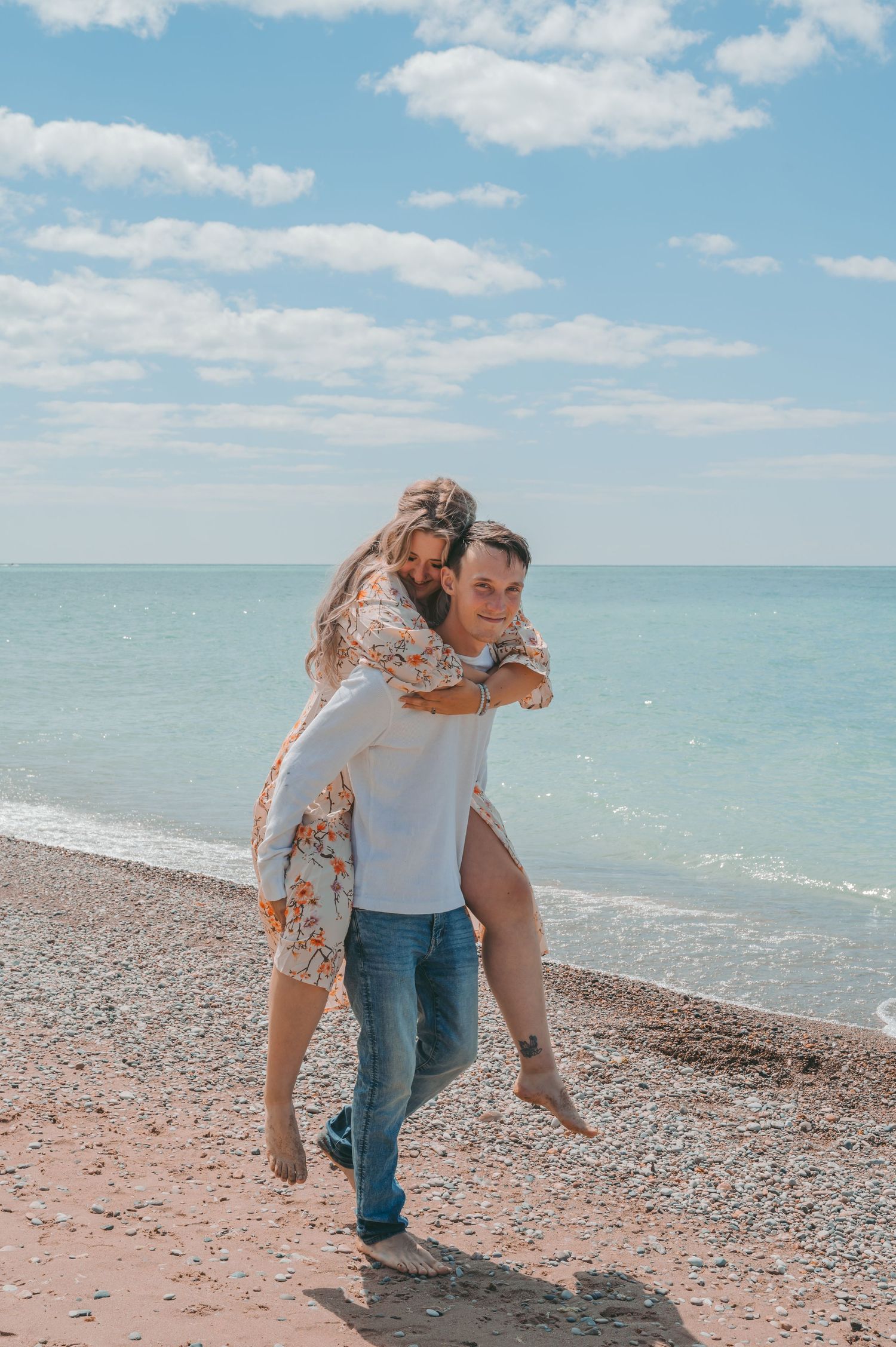 Joyful piggyback ride on sunny beach with floral dress and casual attire.