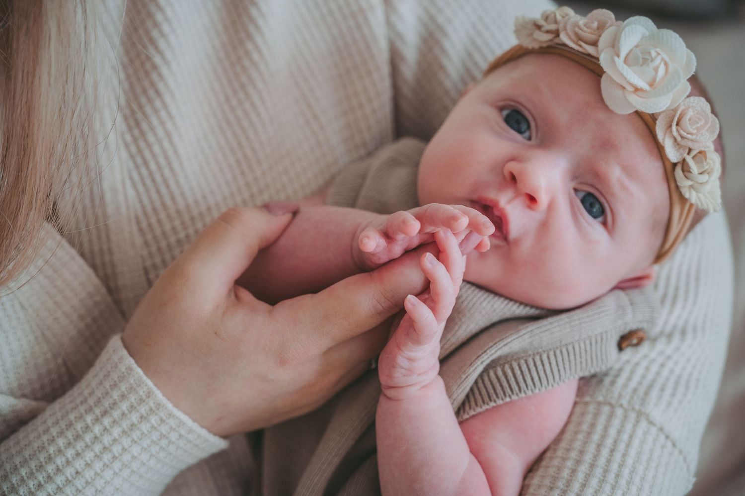 Baby wearing a floral headband sucking on fingers while being cradled in soft knit sweater.