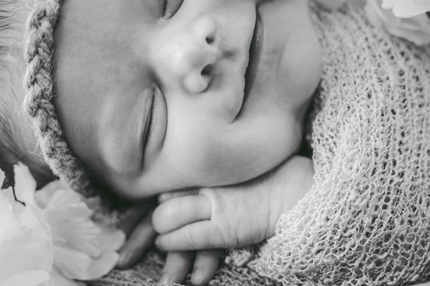 A peaceful close-up of a sleeping newborn wrapped in knit fabric.