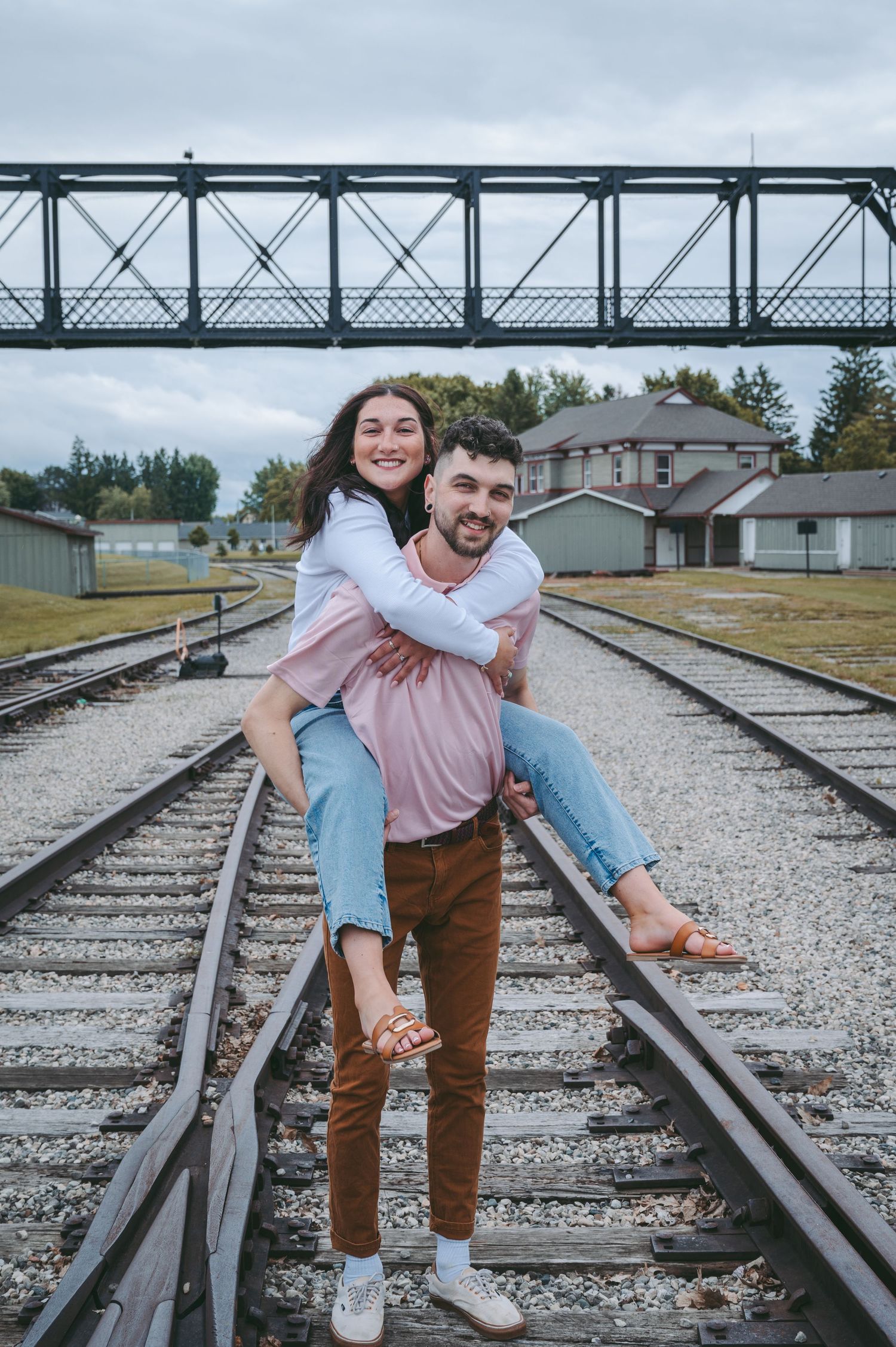 A playful moment captured on train tracks with a metal bridge structure overhead.