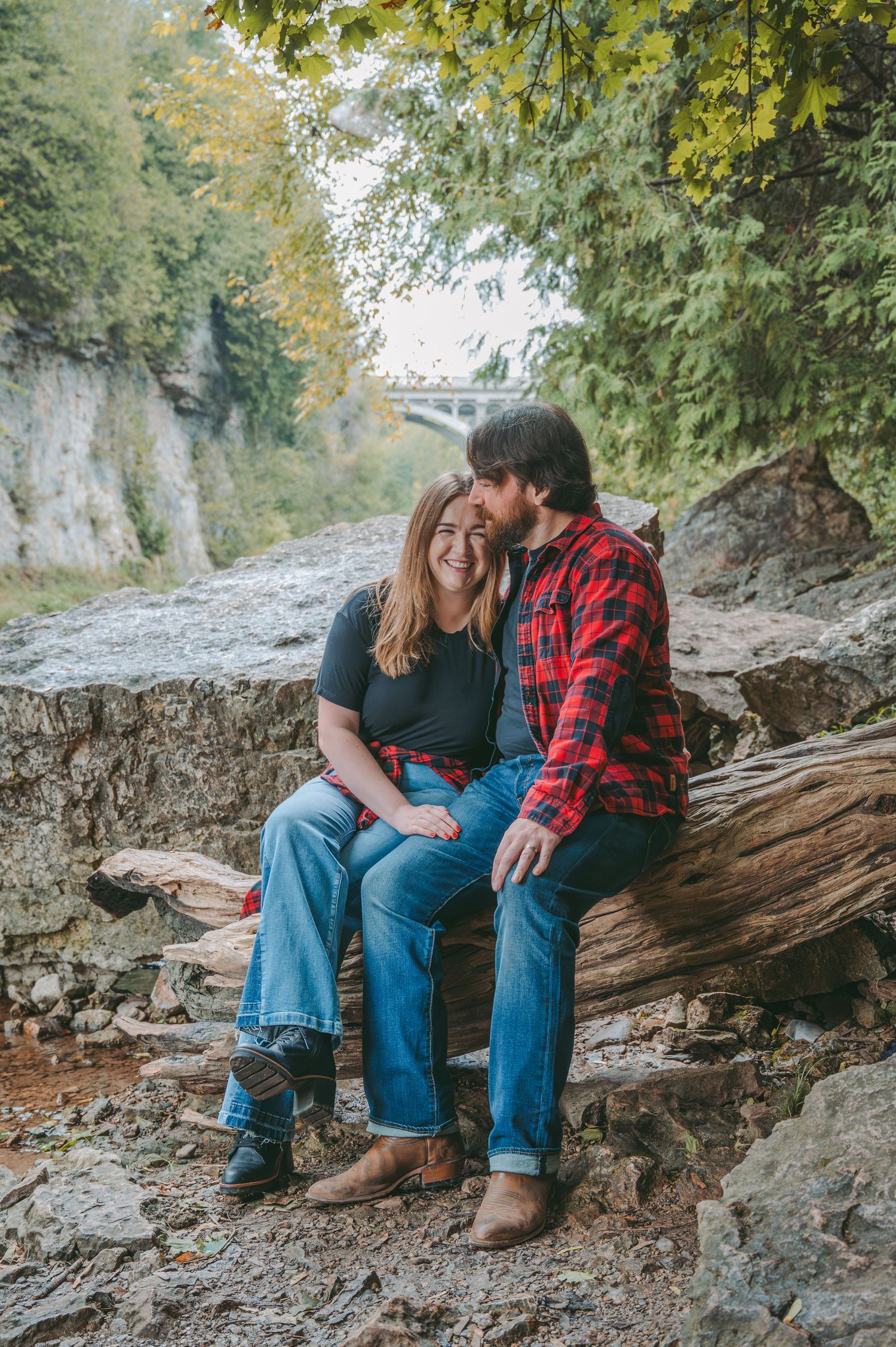 Romantic couple sitting together on rocky cliff overlooking scenic gorge and bridge.