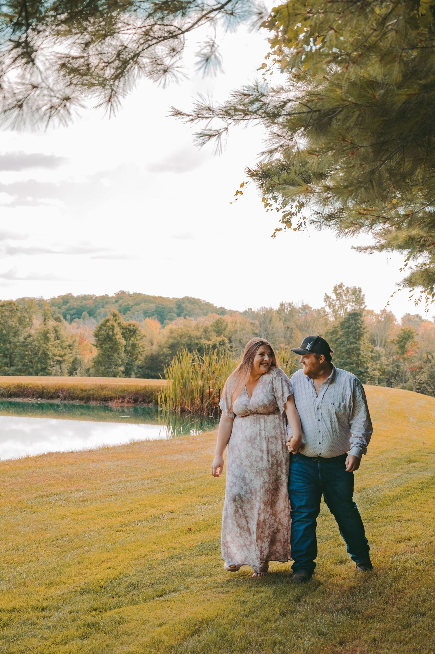 A couple strolls together on a grassy hillside near a serene lake during autumn.