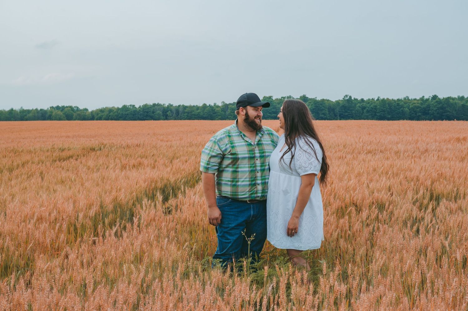 A couple standing close in a golden wheat field at sunset.