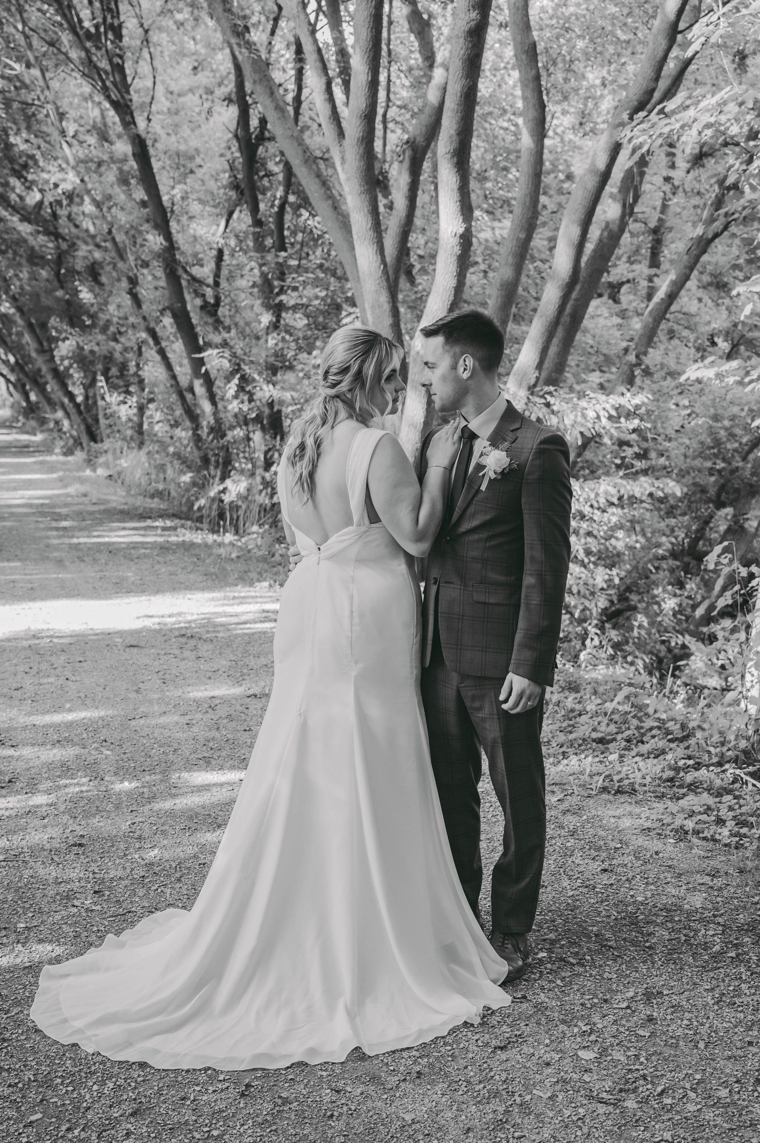 Romantic wedding photos in black and white showing couple walking through tree-lined path.