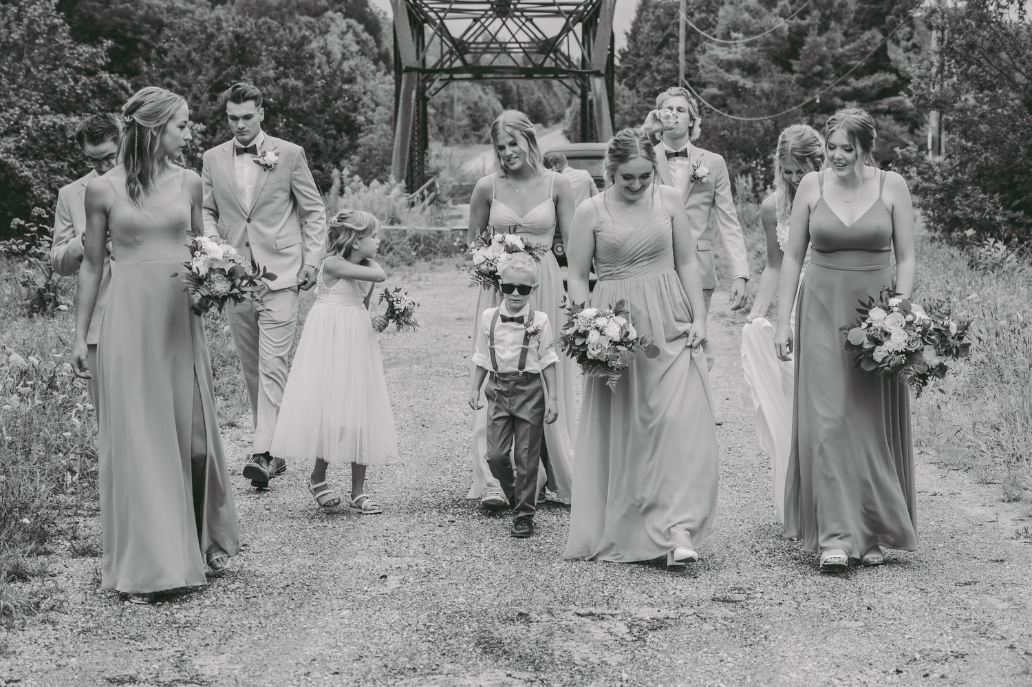 Black and white wedding party photo on rustic bridge with flower bouquets.