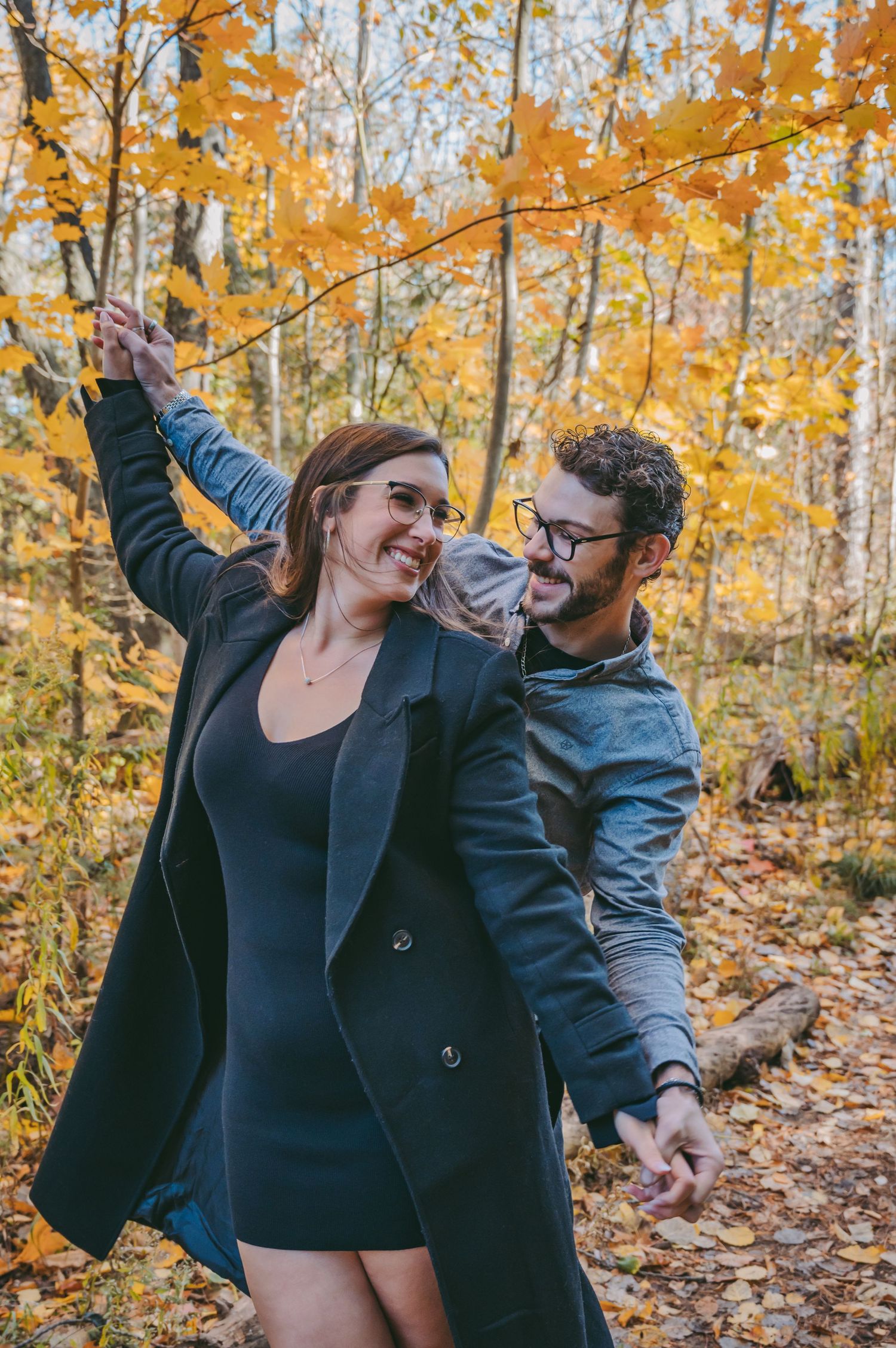 A couple dancing and laughing among fall foliage on an autumn day.