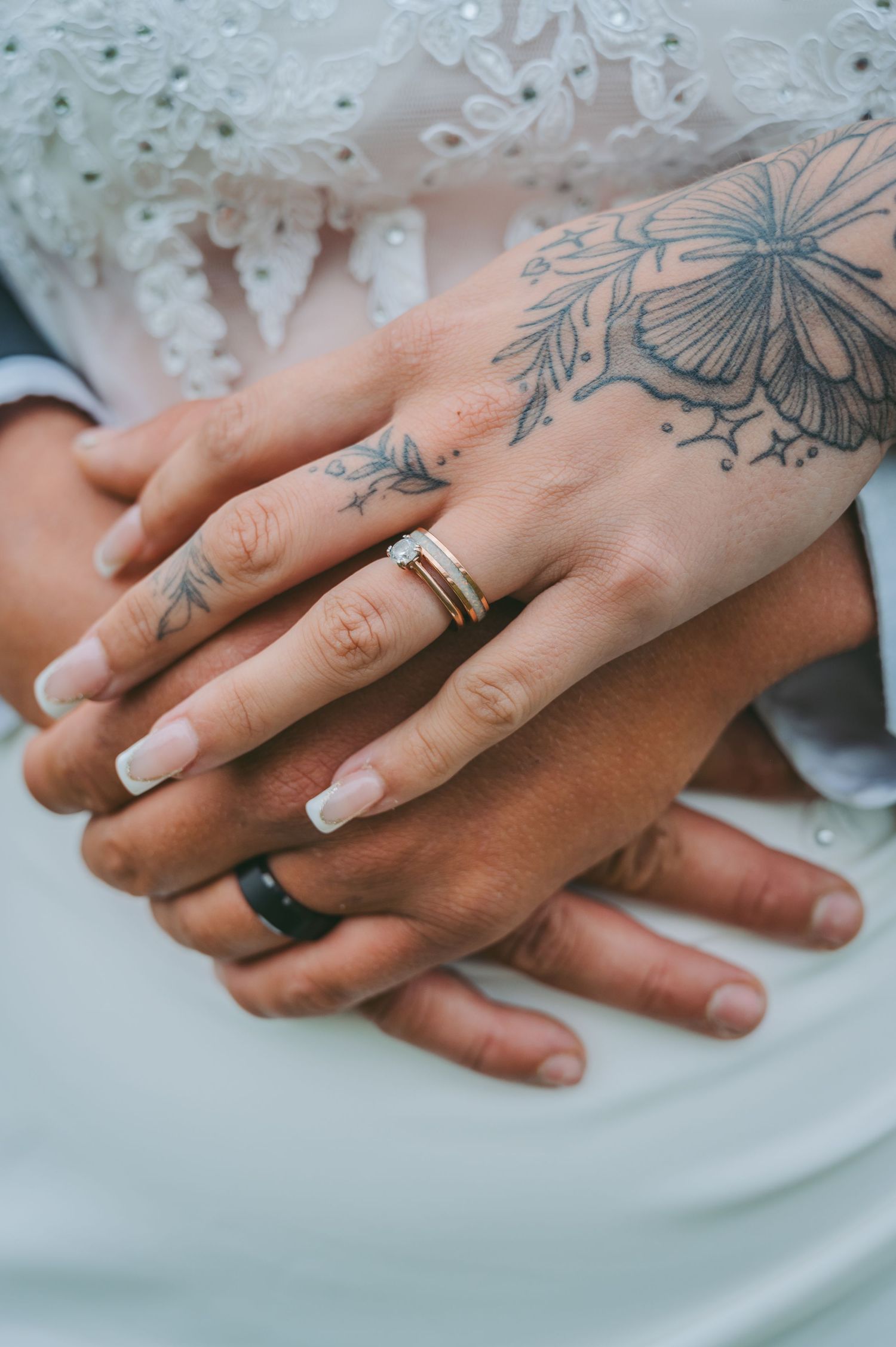 Close-up of newlyweds' hands with wedding rings and butterfly tattoo artwork.