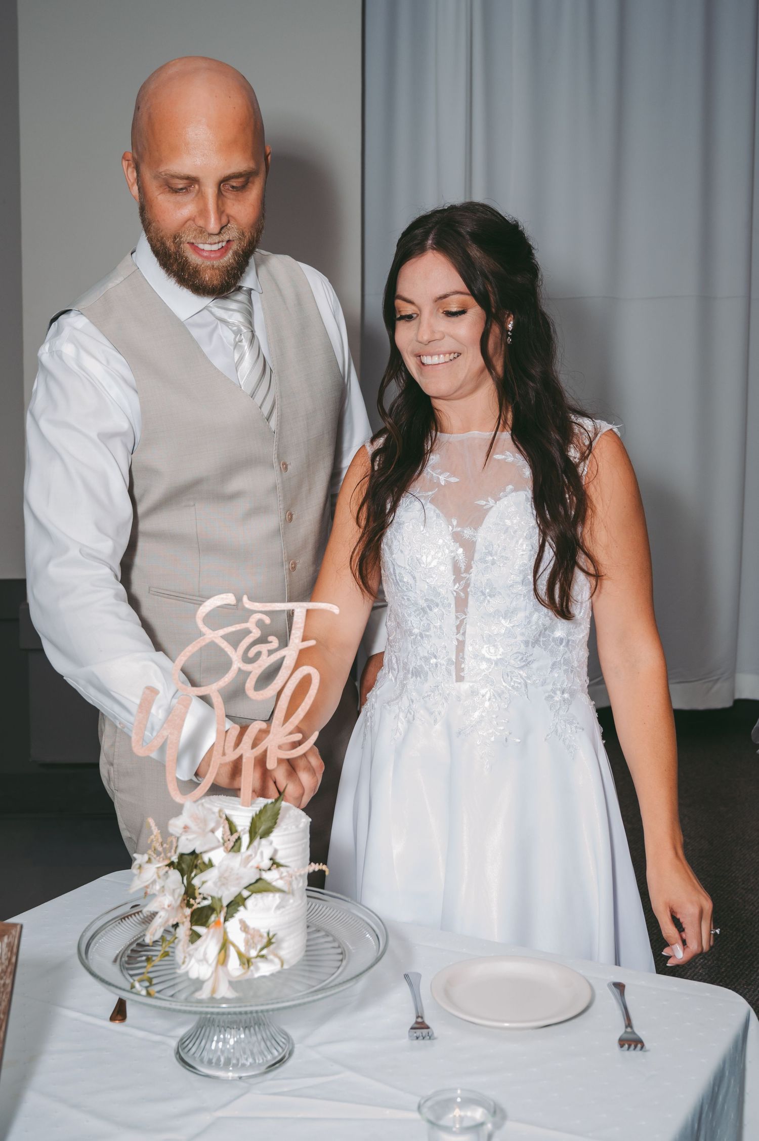 A couple cuts their wedding cake together with a neon 'Get Wild' sign displayed on an elegant silver cake stand.