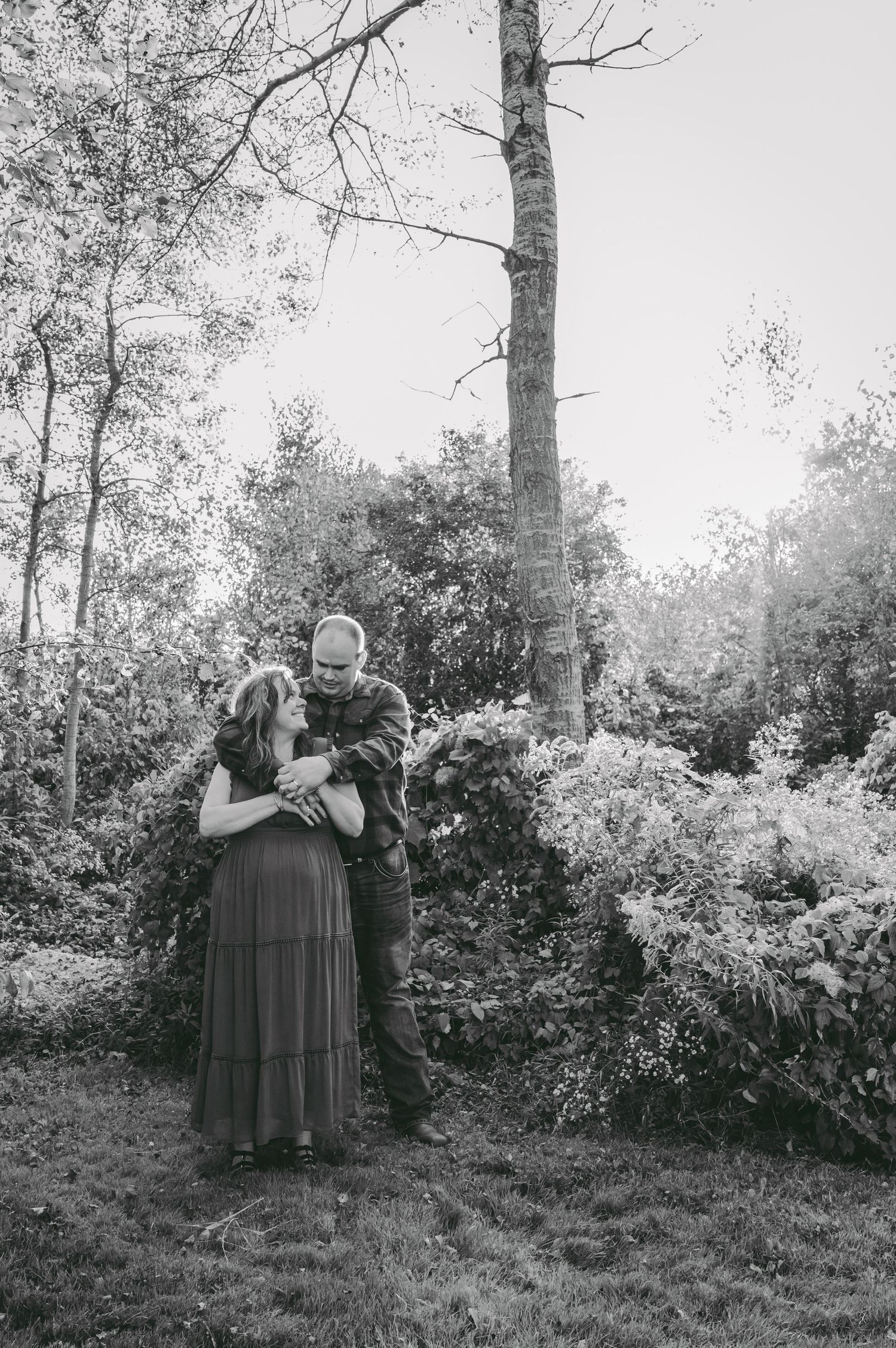 A black and white portrait of a couple embracing in a wooded setting.