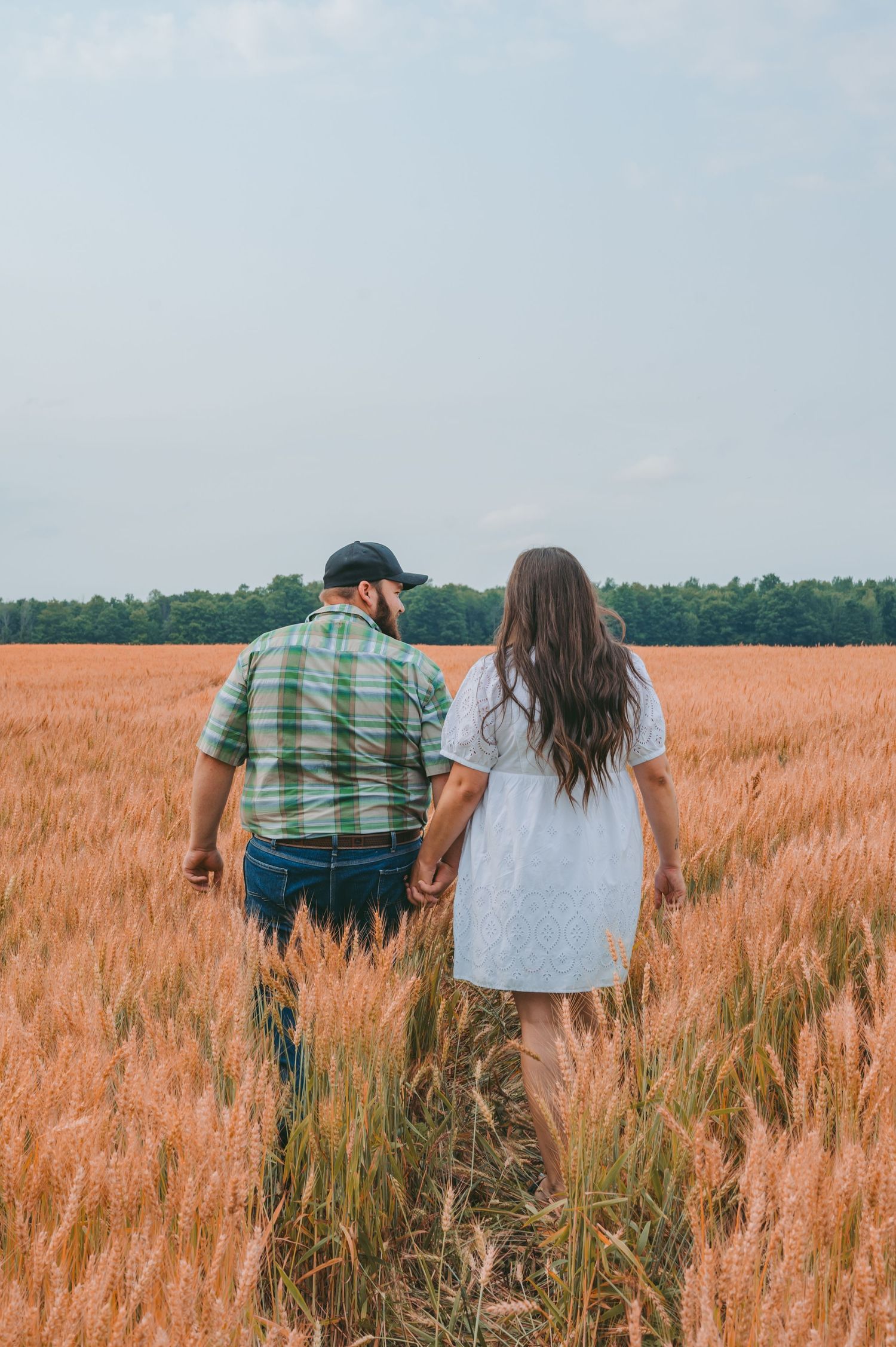 A couple walking hand in hand through a serene wheat field on a summer day.
