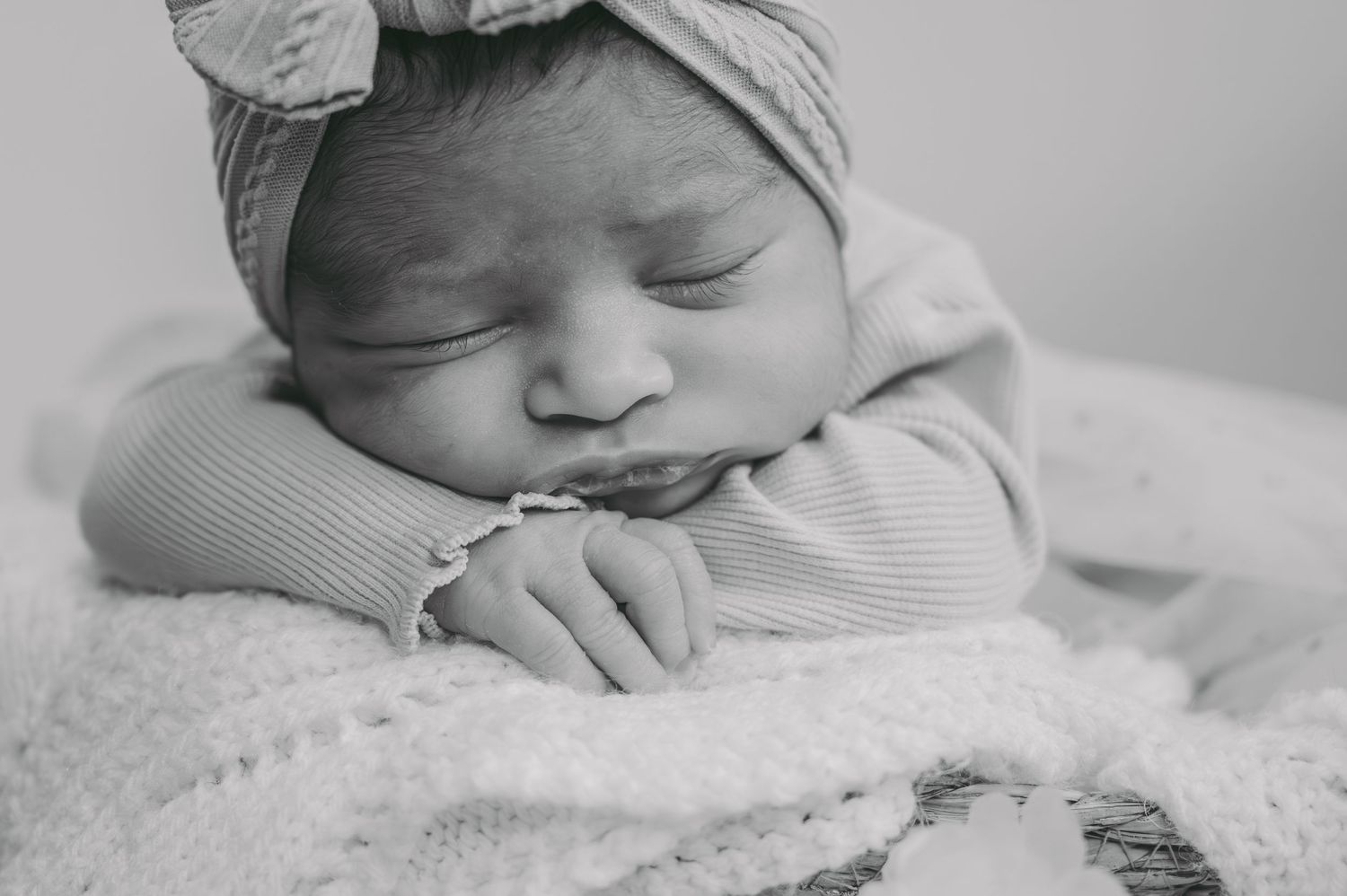 Sleeping newborn baby wearing a headwrap rests peacefully on a white blanket in black and white.