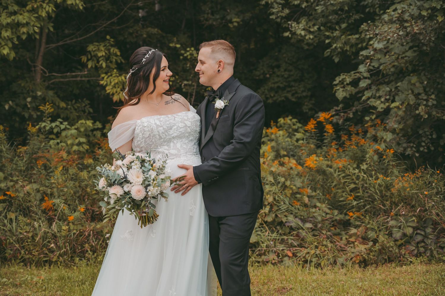 A romantic outdoor wedding photo with a couple embracing in a garden setting with autumn foliage and flowers.
