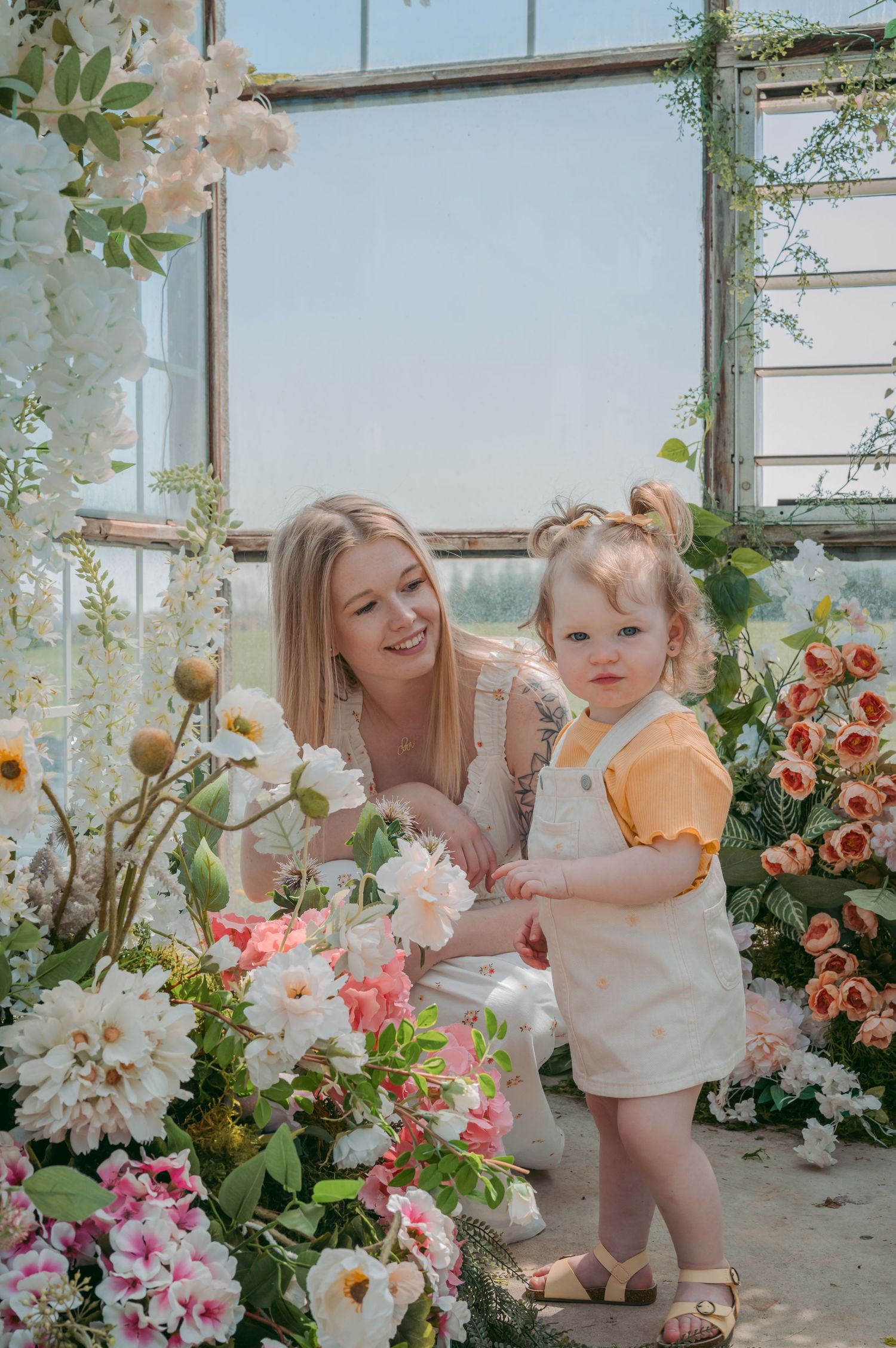Mother and child explore beautiful greenhouse filled with blooming flowers and climbing vines.