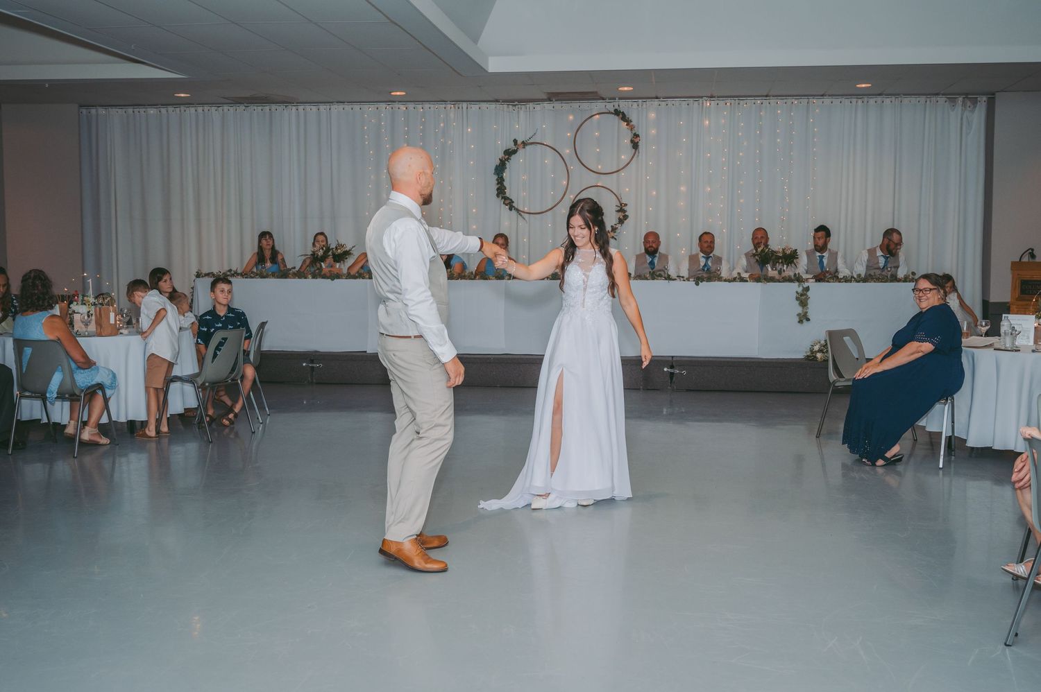 First dance between newlyweds on white dance floor at indoor reception.