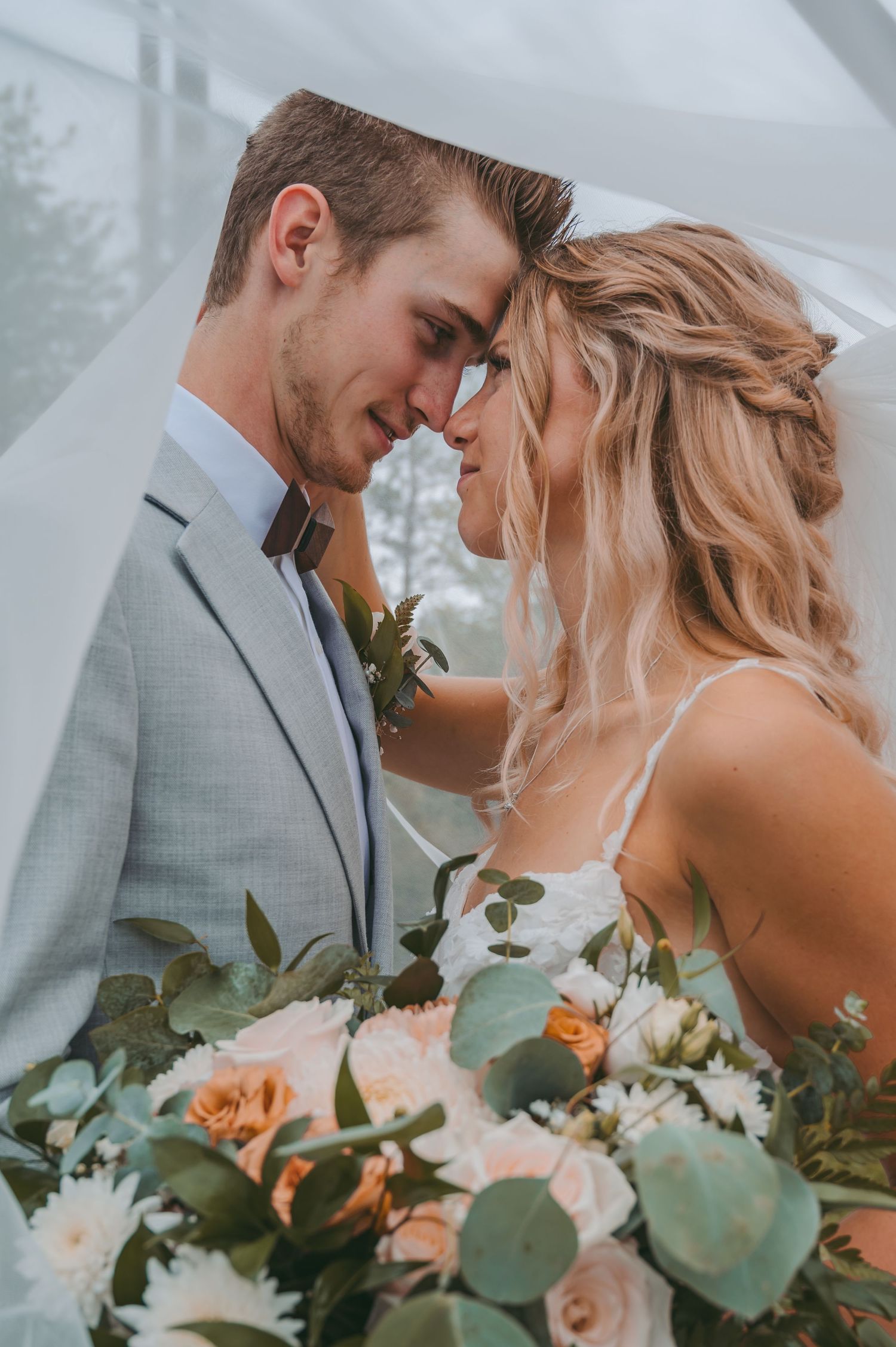 Romantic close-up of couple sharing intimate moment with peach and white floral bouquet.