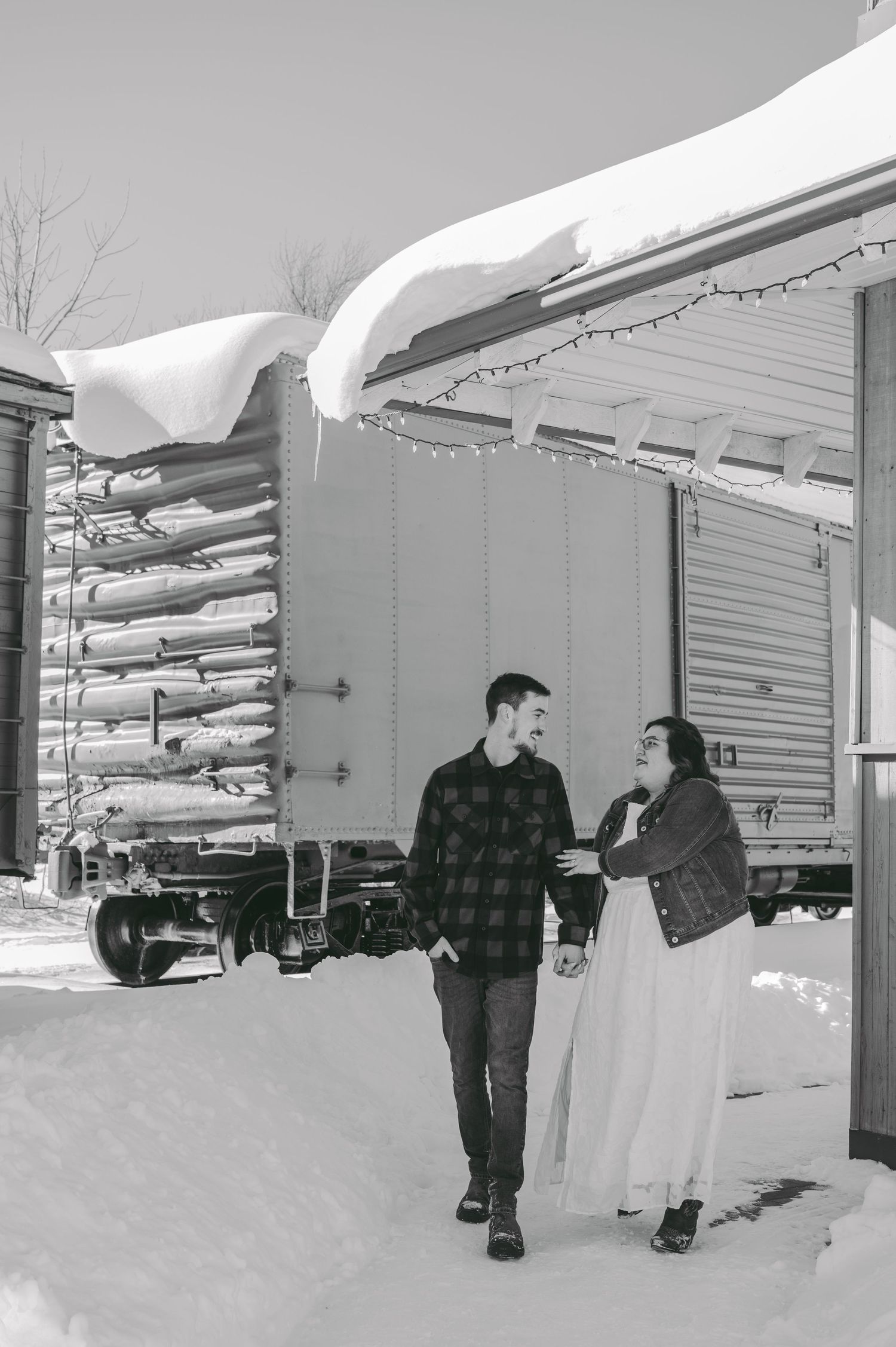 Couple walking together in snowy winter scene with snow-covered buildings.