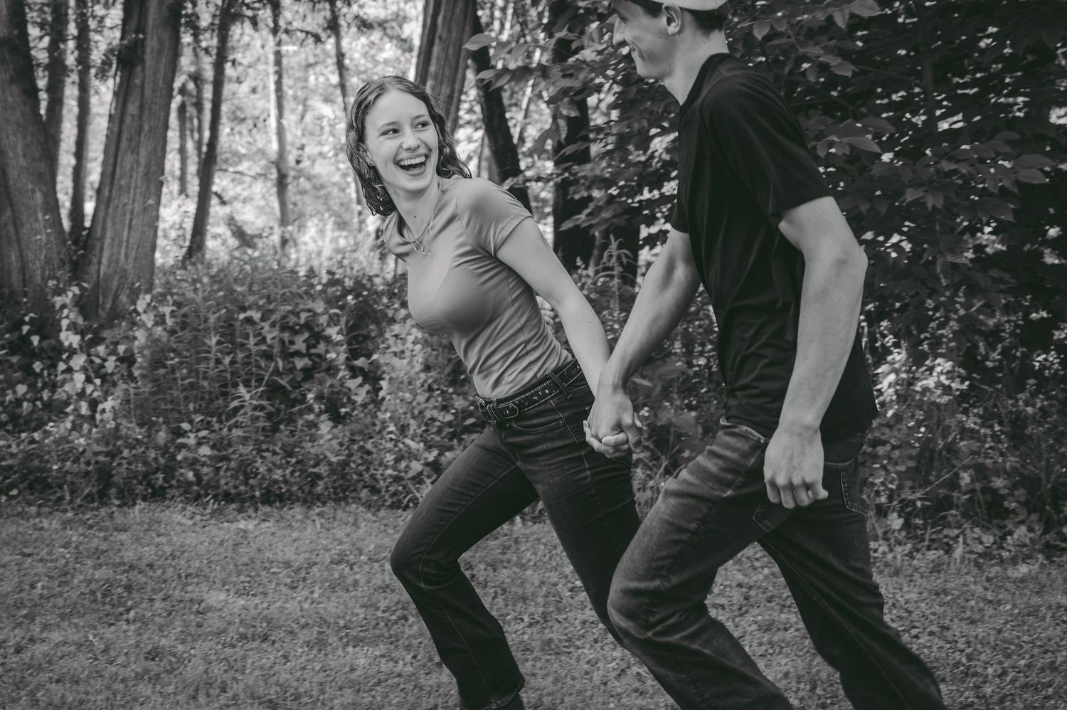 A candid black and white photo capturing a joyful moment between a couple in a natural outdoor setting.