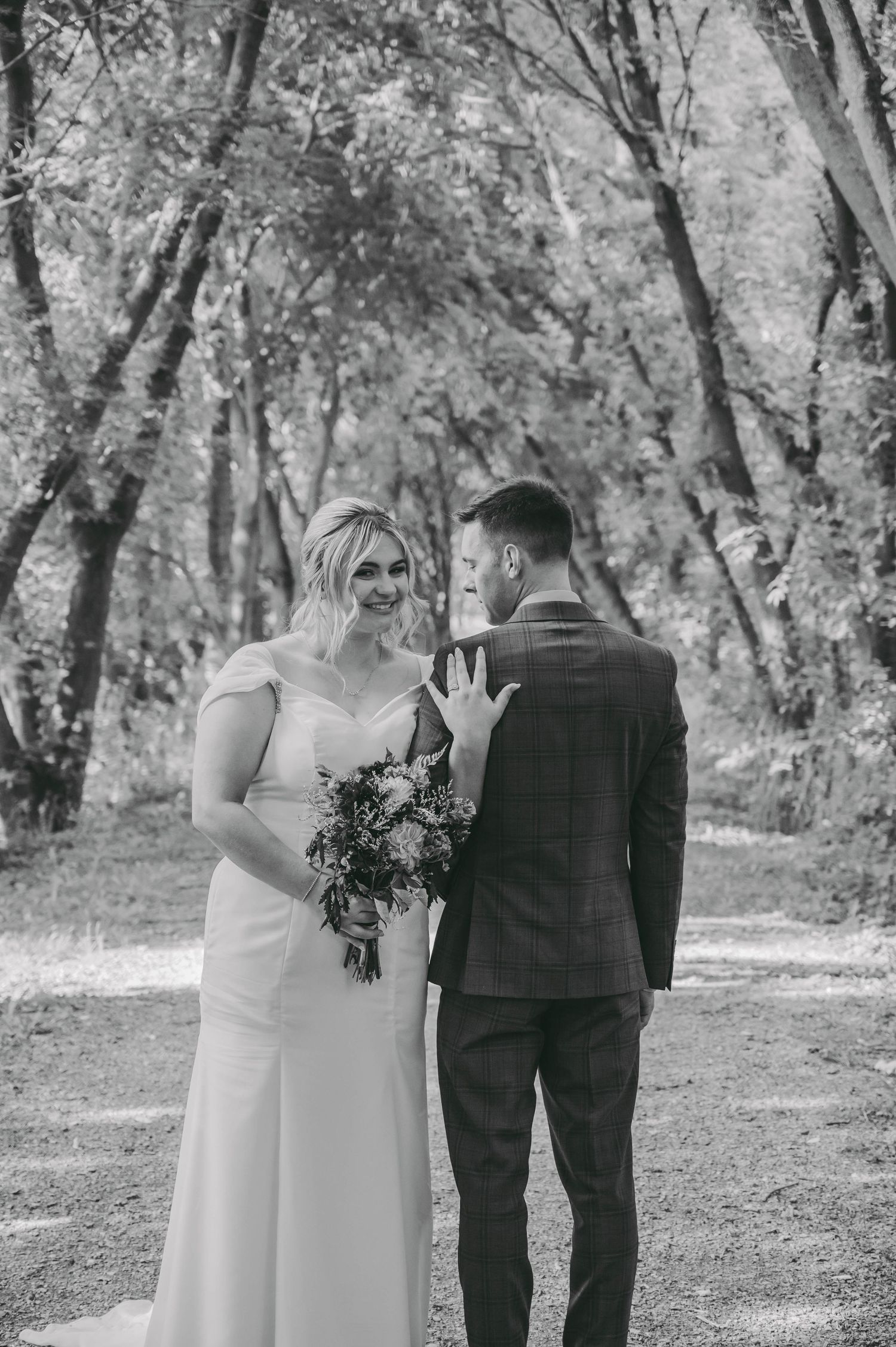 Wedding couple walking together on wooded path in black and white photography.