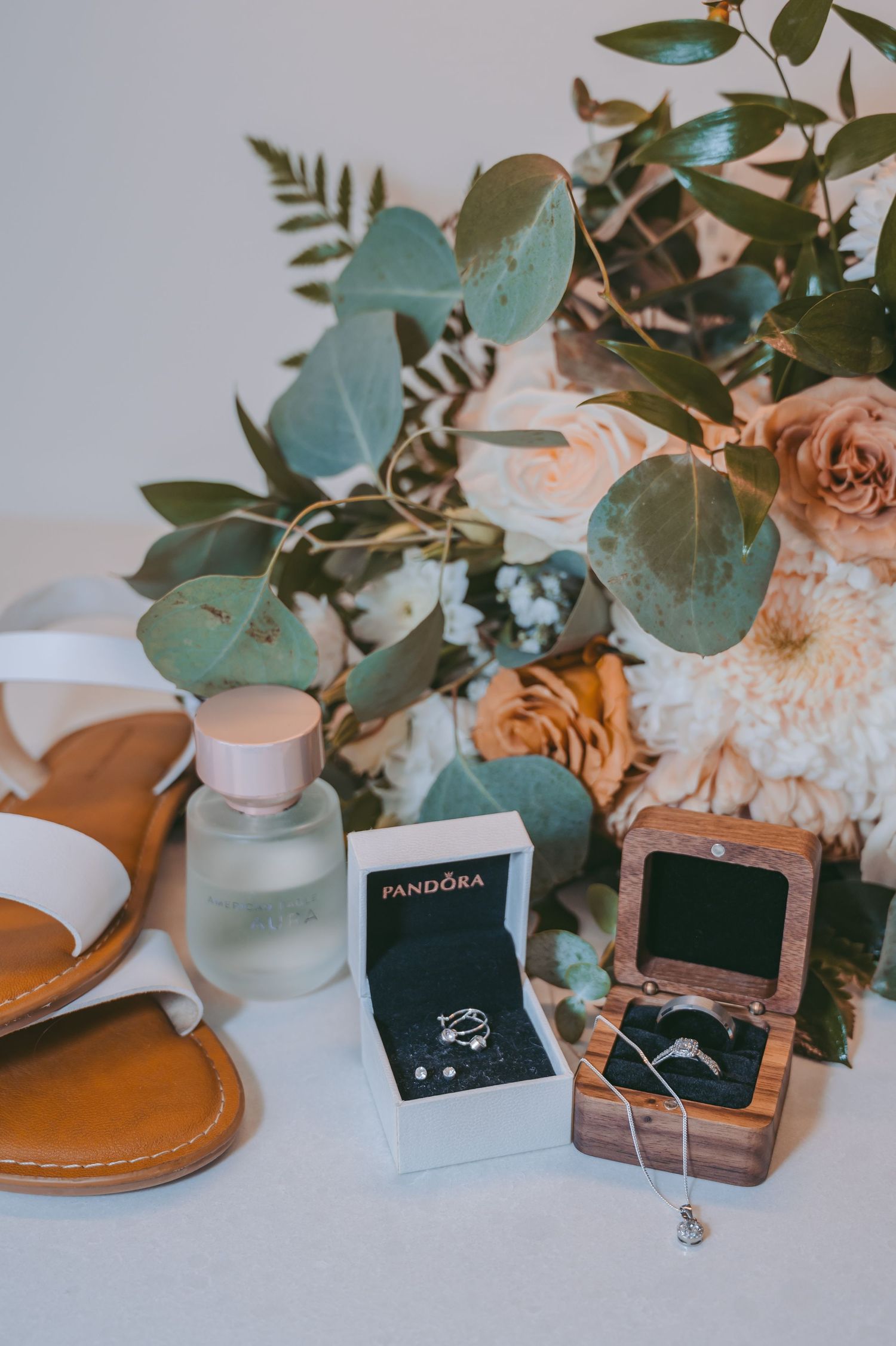 Wedding jewelry and accessories artfully arranged with eucalyptus leaves on light background.