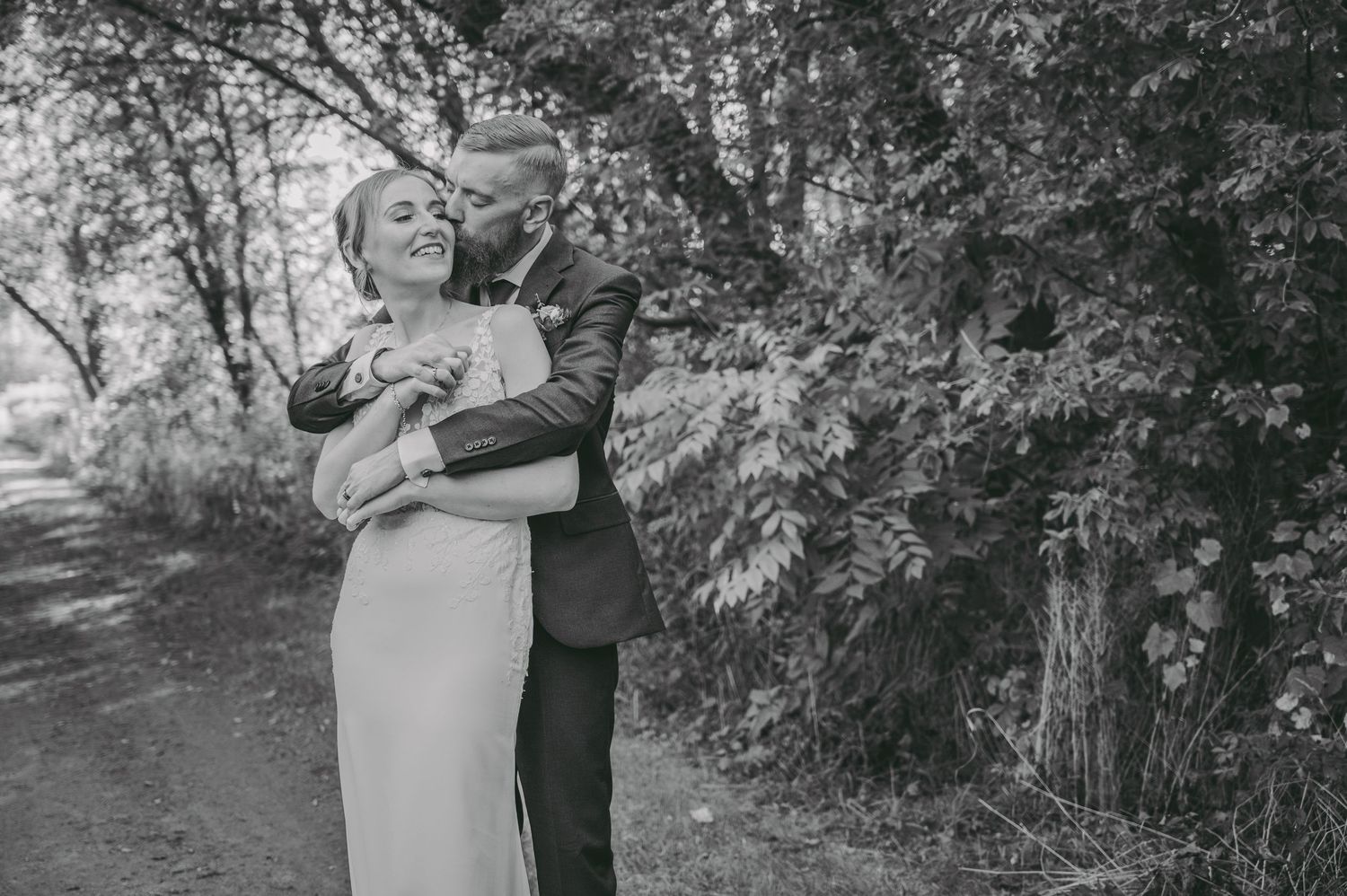 Black and white intimate wedding portrait showing a tender embrace in a wooded setting.