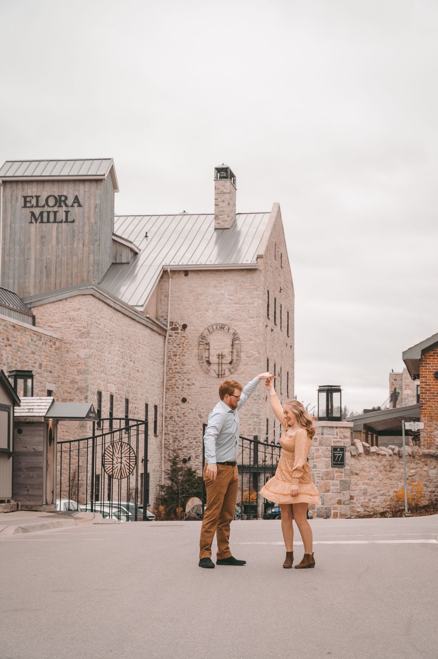 Couple stands facing each other outside historic Flour Mill building on overcast day.