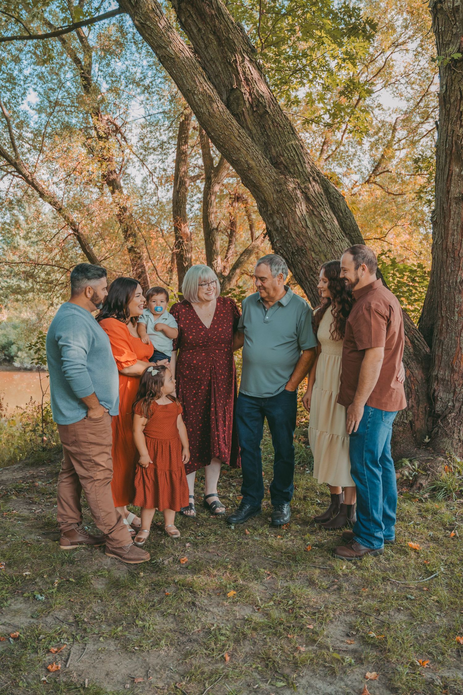 Extended family gathering poses together under trees during autumn photo session.