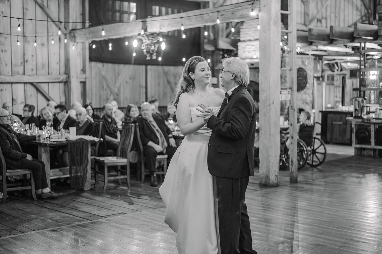 Black and white photo of a bride and older man sharing a father-daughter dance at a rustic barn wedding reception.