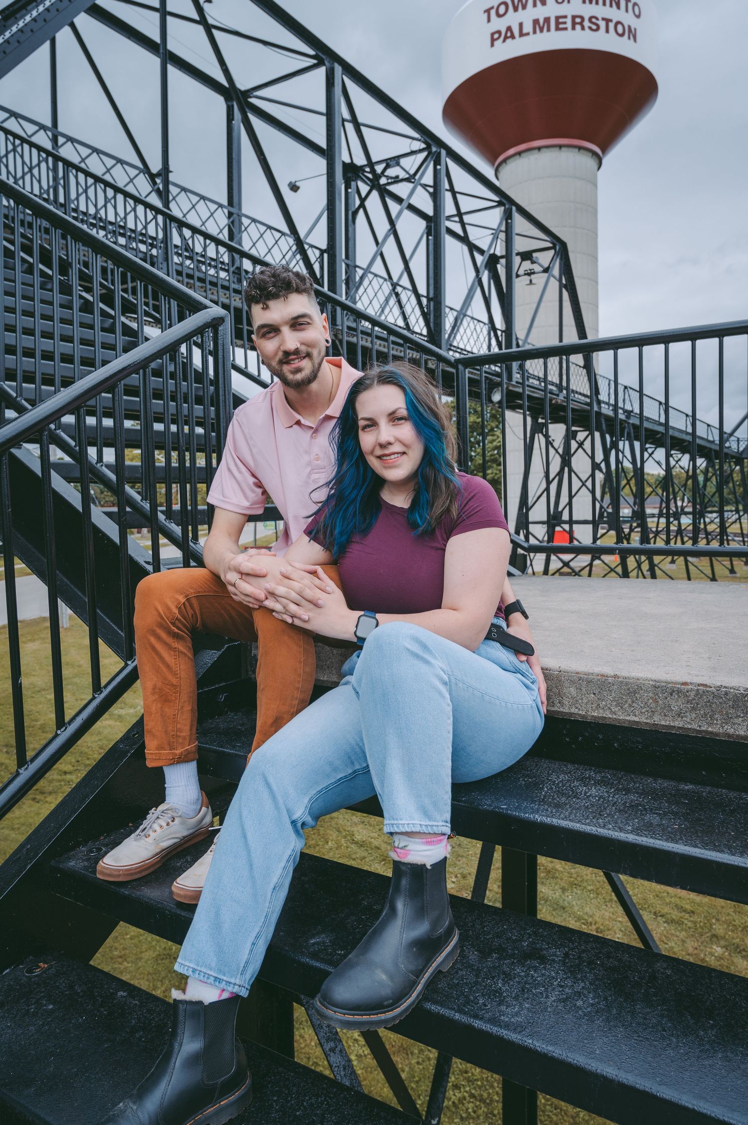 A couple sits on metal stairs with a distinctive water tower visible in the background.