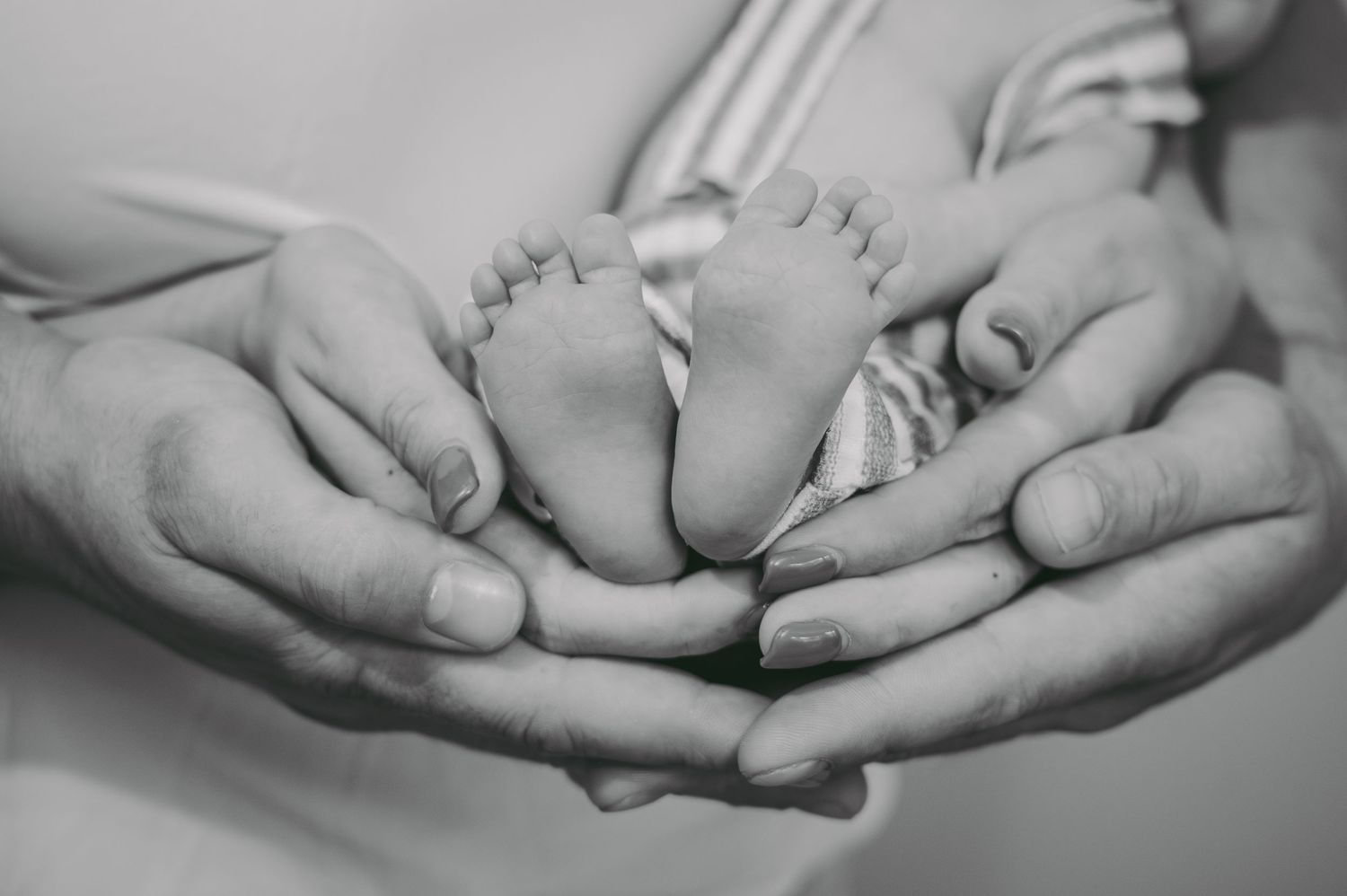 Black and white close-up of tiny newborn feet cradled in adult hands.