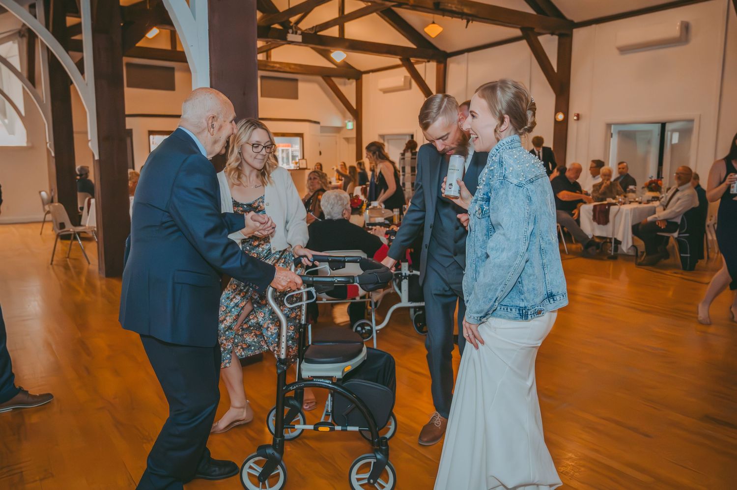 Wedding guests gather around and interact during reception in rustic wooden beam venue.