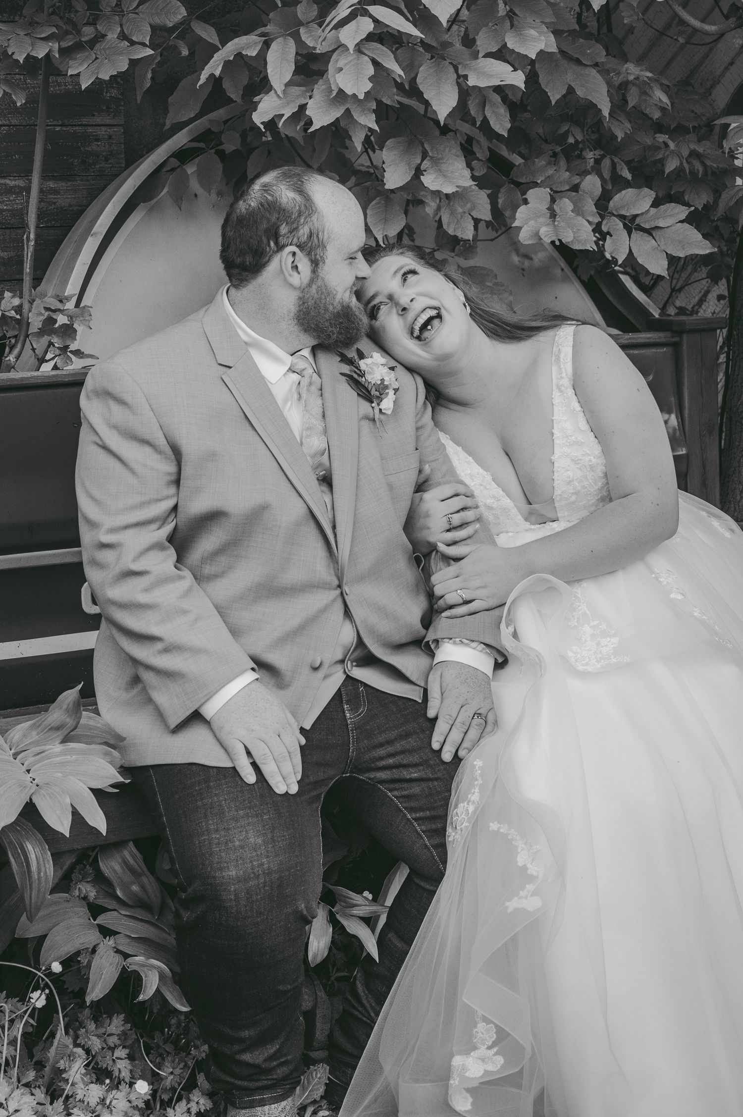 A joyful moment captured between newlyweds sharing laughter under leafy foliage.