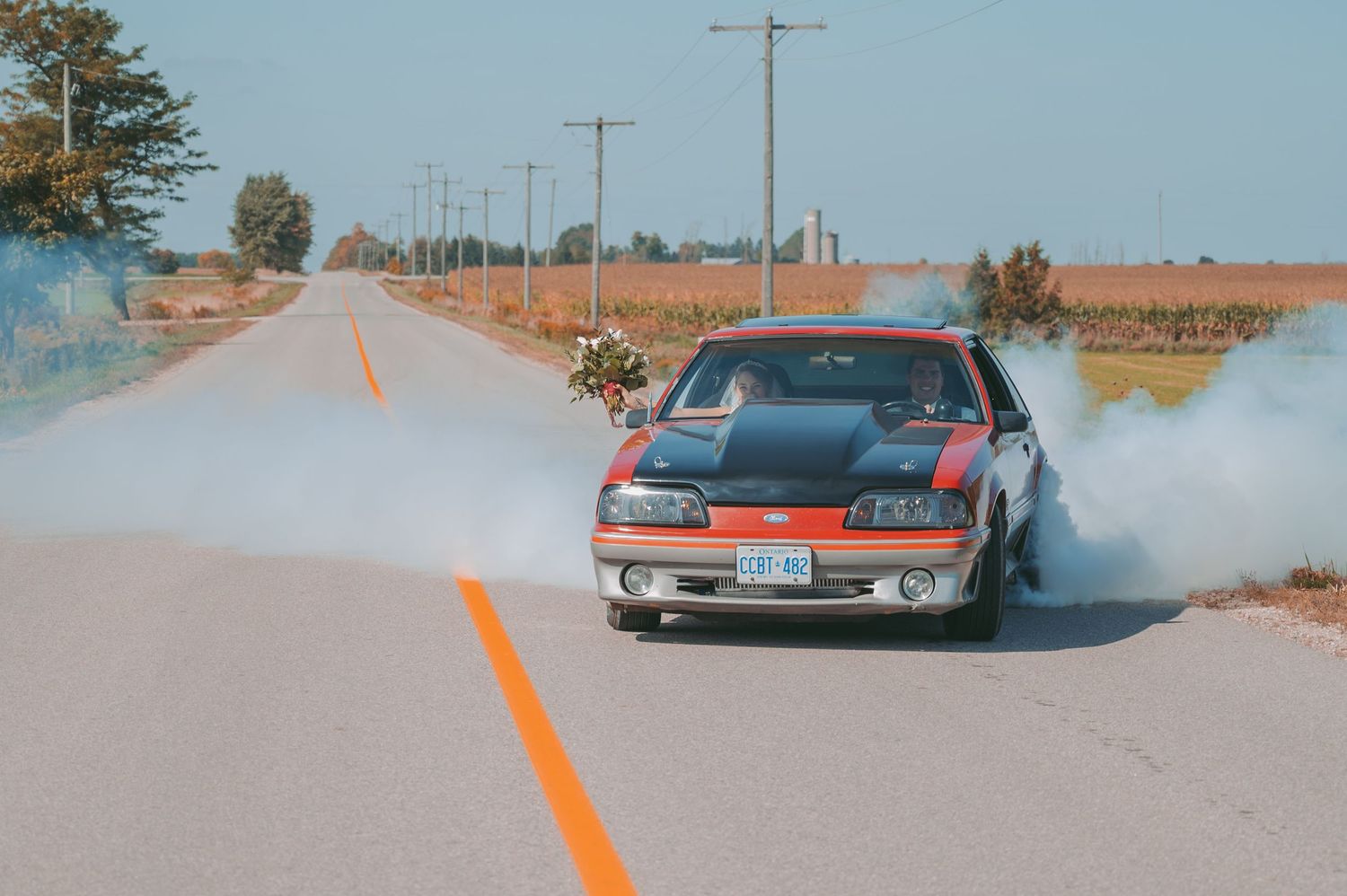 Vintage car doing a burnout on country road with blue sky background.