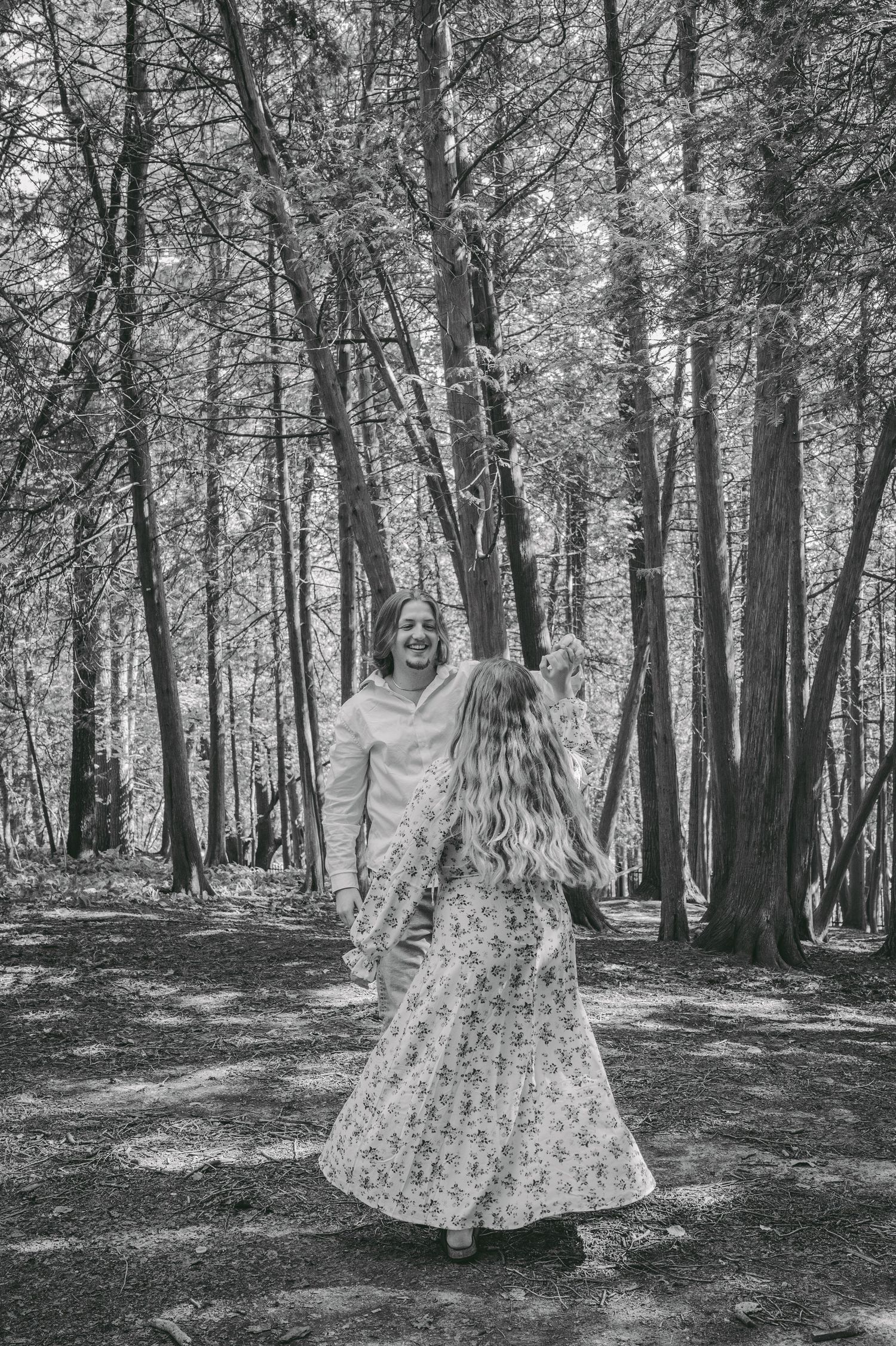A romantic black and white portrait of a couple standing among tall trees in a forest.
