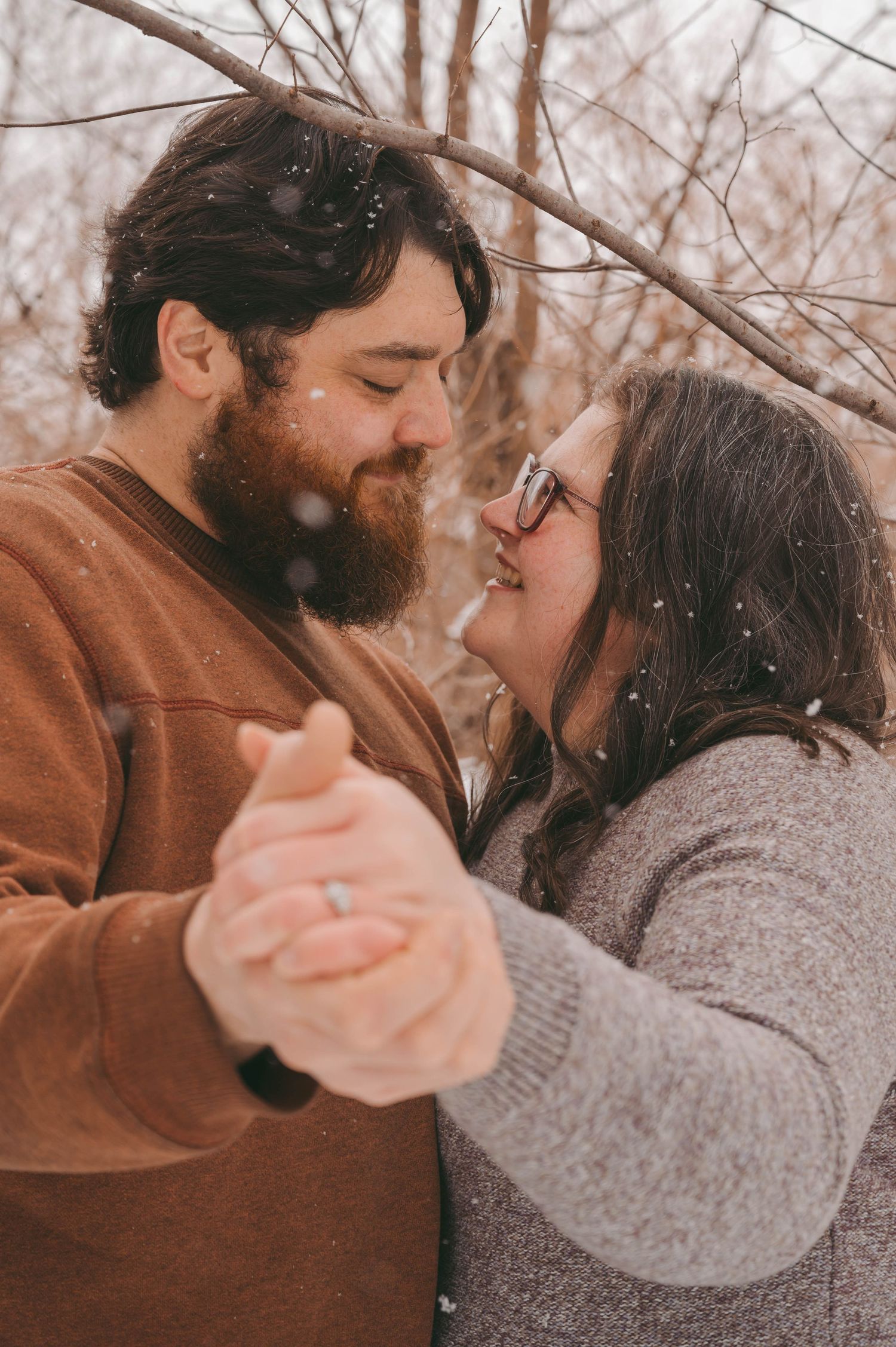 A couple dancing and laughing together during a snowy winter photoshoot.