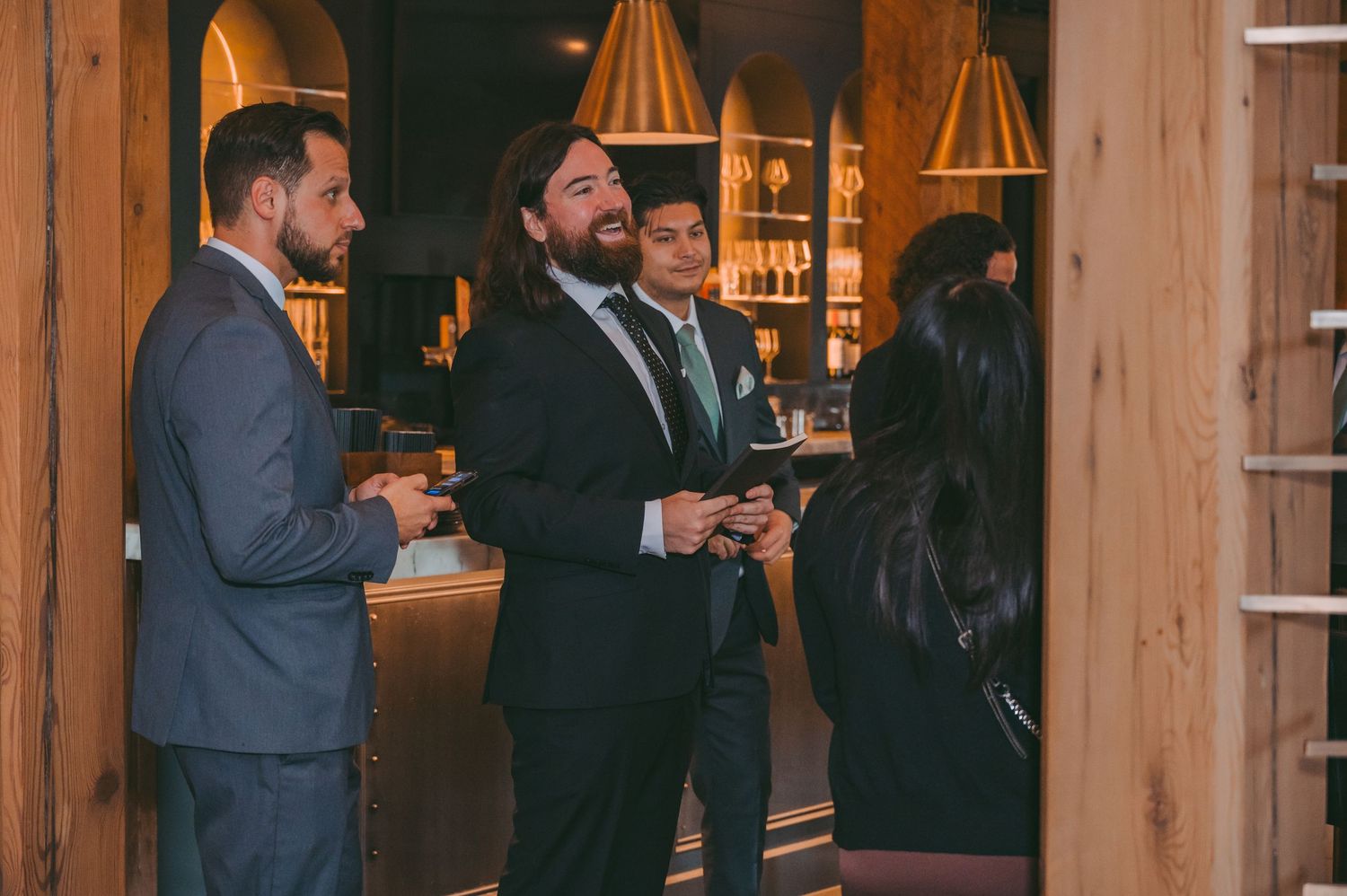 Wedding reception guests mingling in rustic venue with wooden beams and warm lighting.