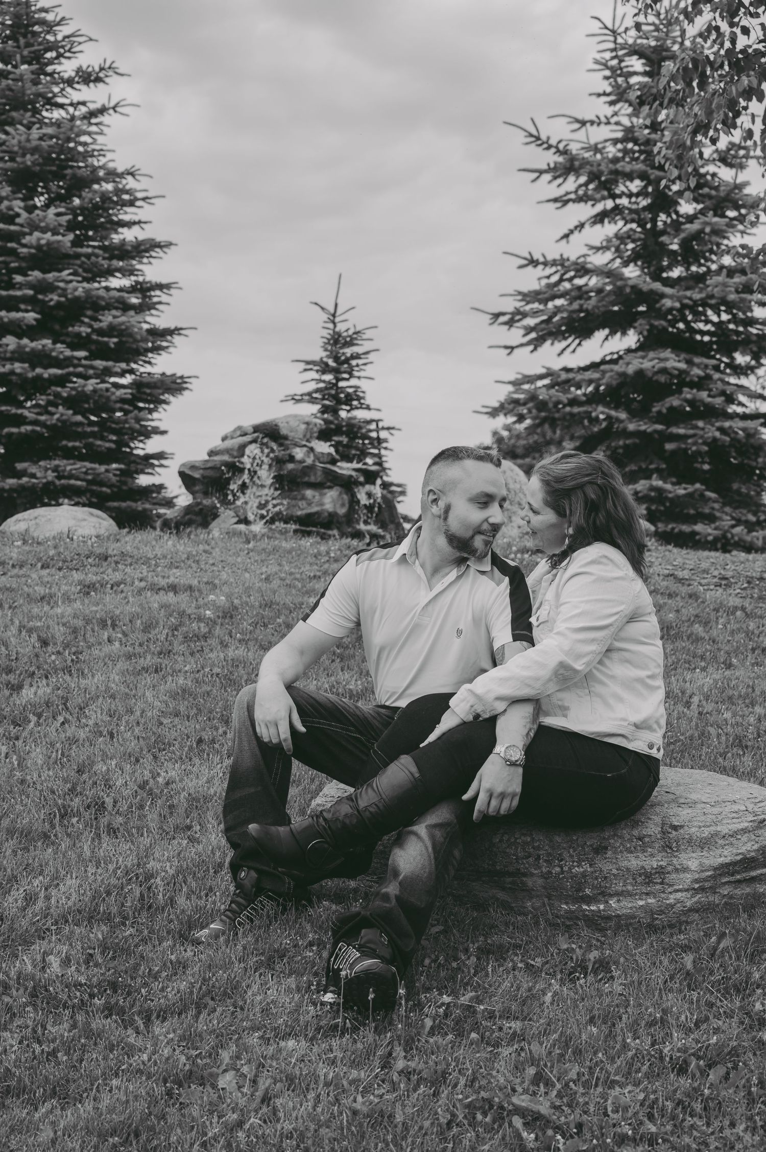 A couple sitting together on a rock surrounded by evergreen trees.