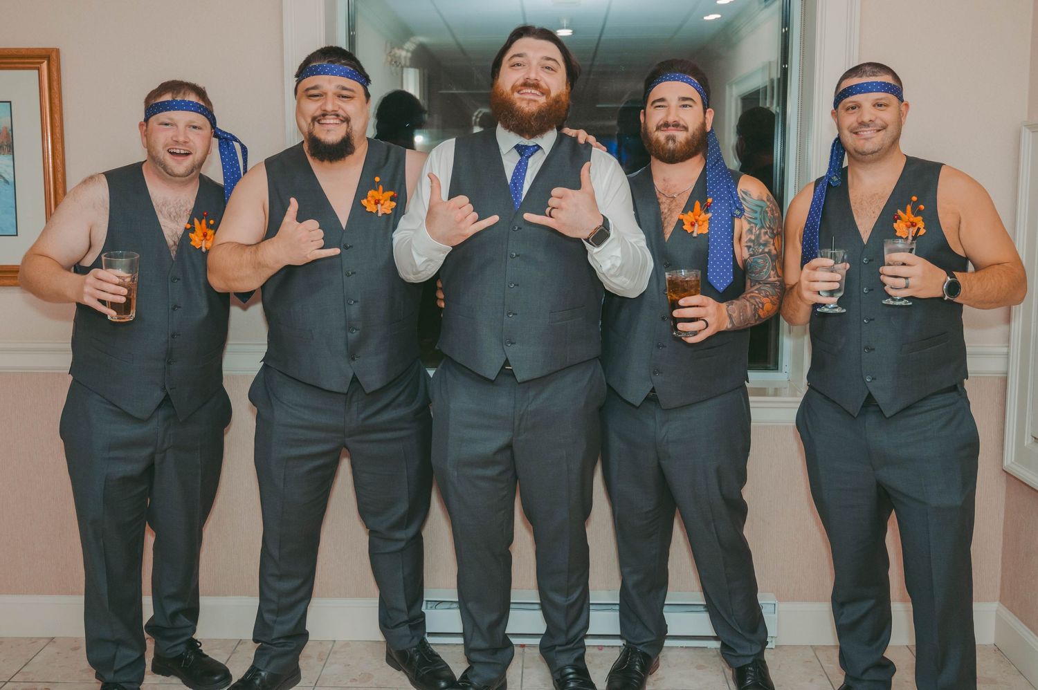 Wedding party members posing in matching formal attire in venue hallway.