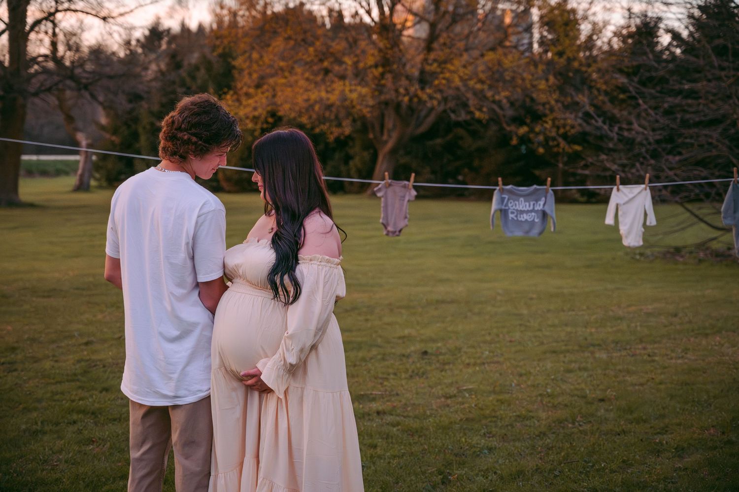 Couple looking at baby clothes hanging on a clothesline in their backyard at sunset.