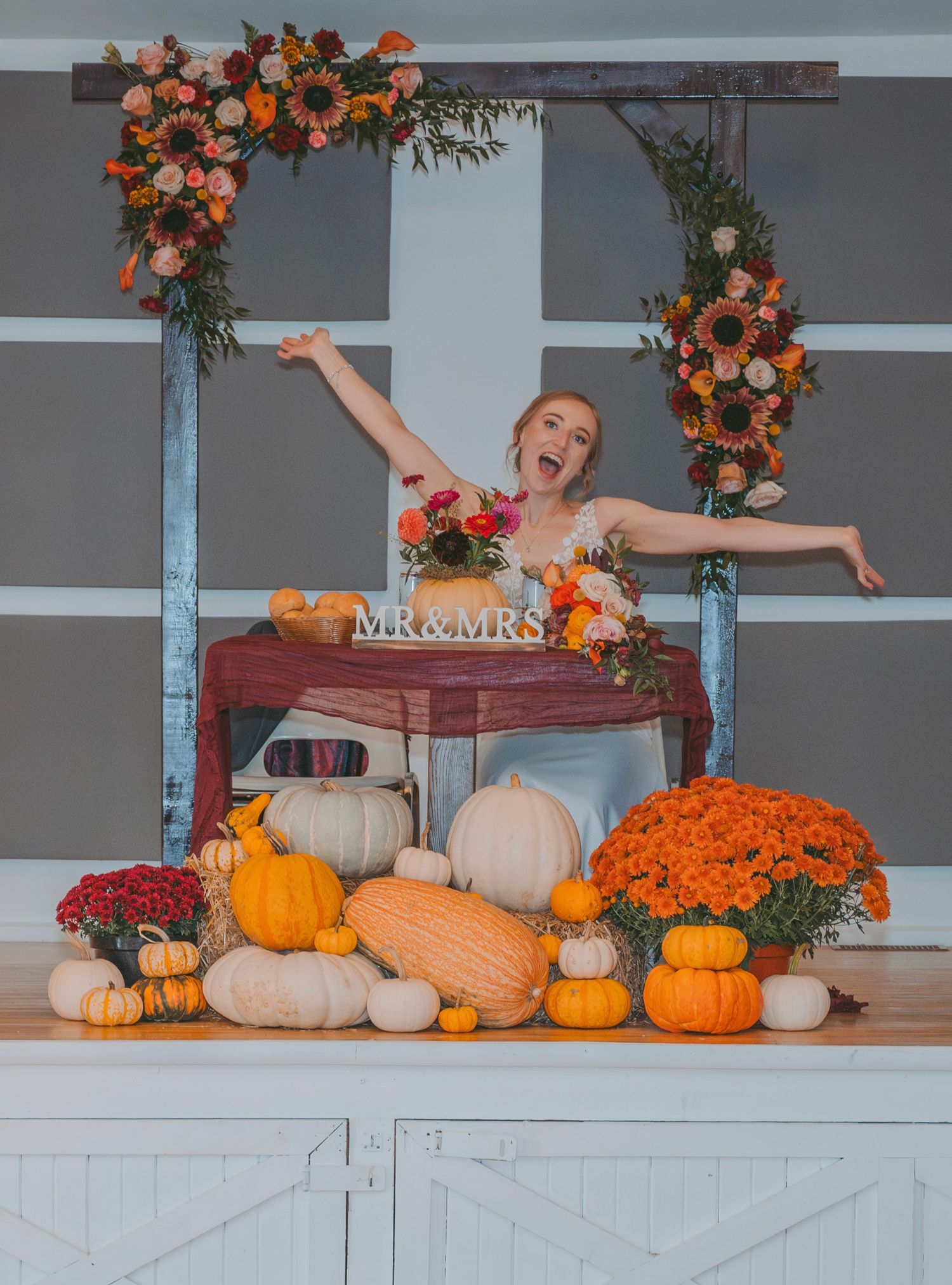 A festive fall display with orange and white pumpkins, floral arrangements, and decorative elements with the bride posing.
