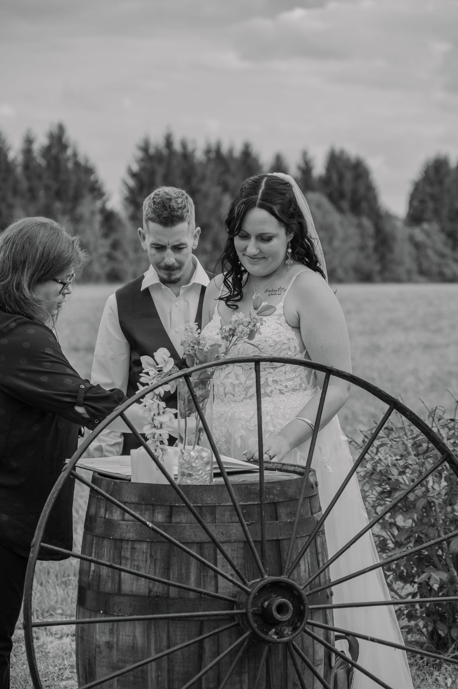 Black and white photos show bride and groom gathering around a rustic wooden wagon wheel in a countryside setting.