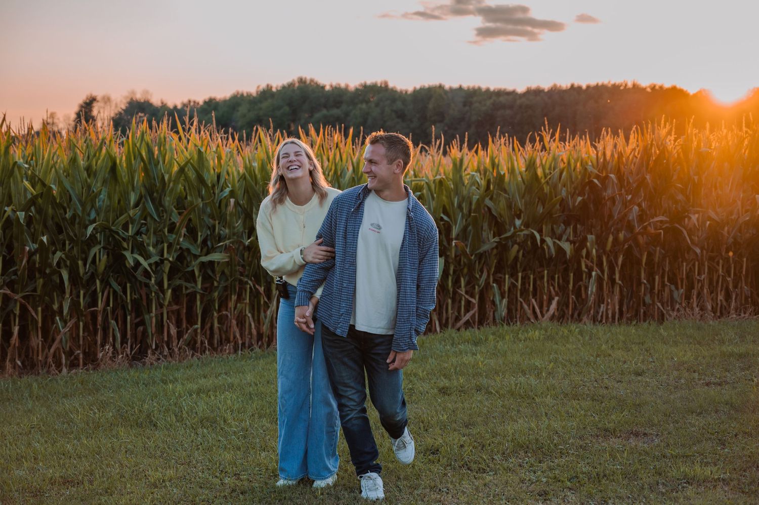 People walking through tall golden grass during sunset in a cornfield.