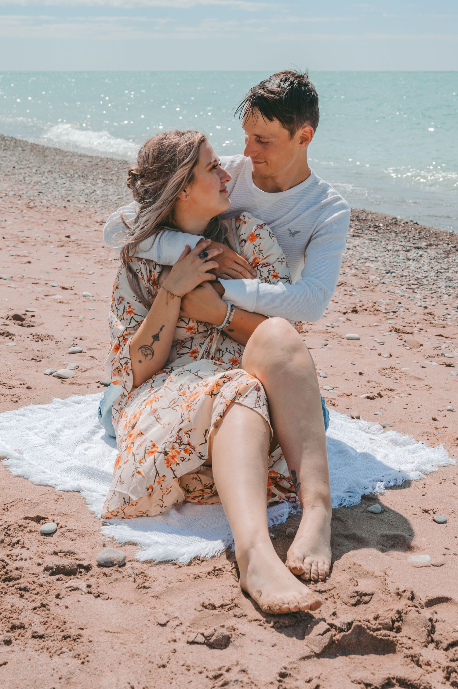 Romantic couple sits on a blanket at the beach sharing an intimate moment against turquoise waters.