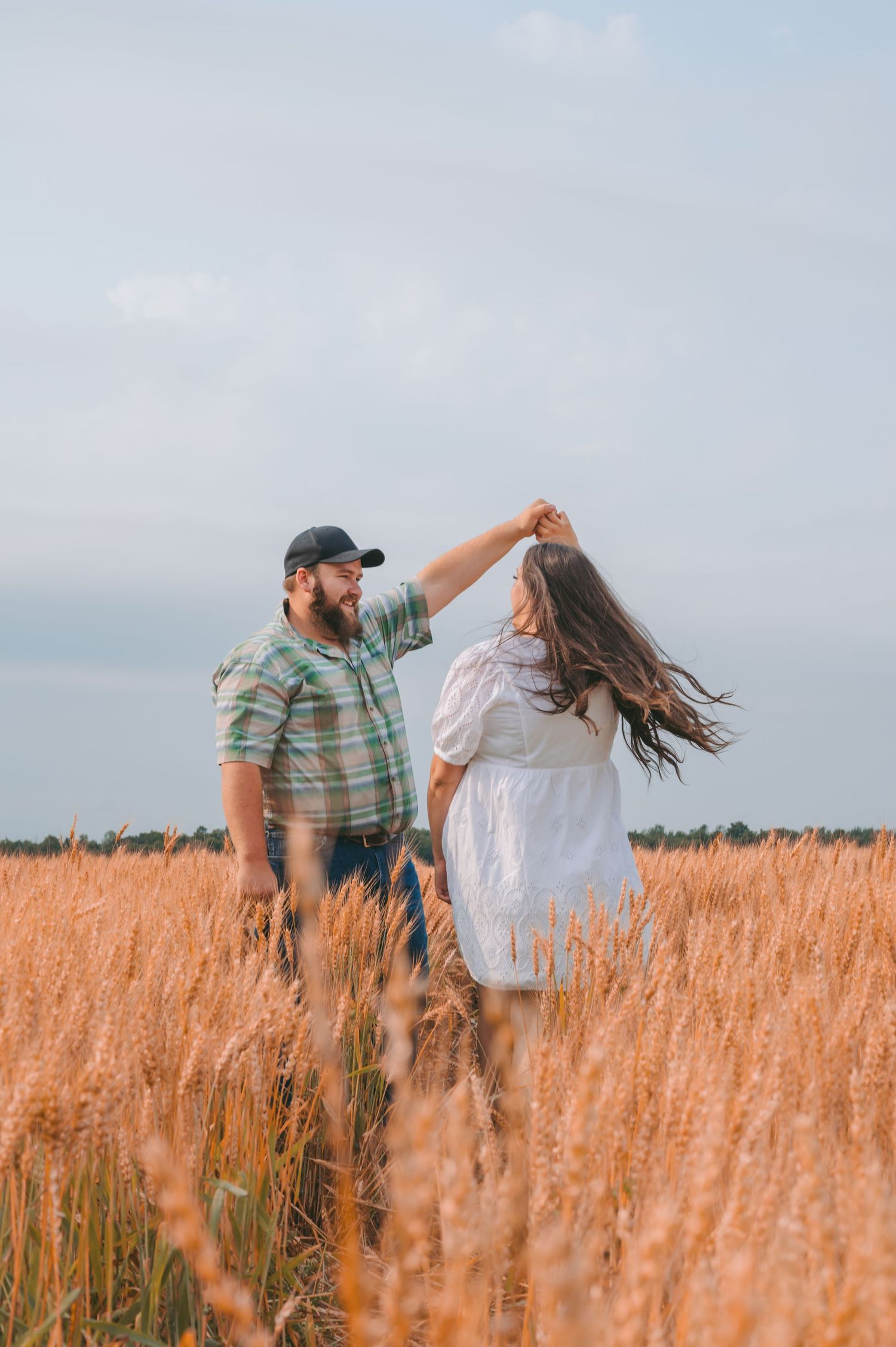 A couple dancing and twirling in a golden wheat field on a cloudy summer day.