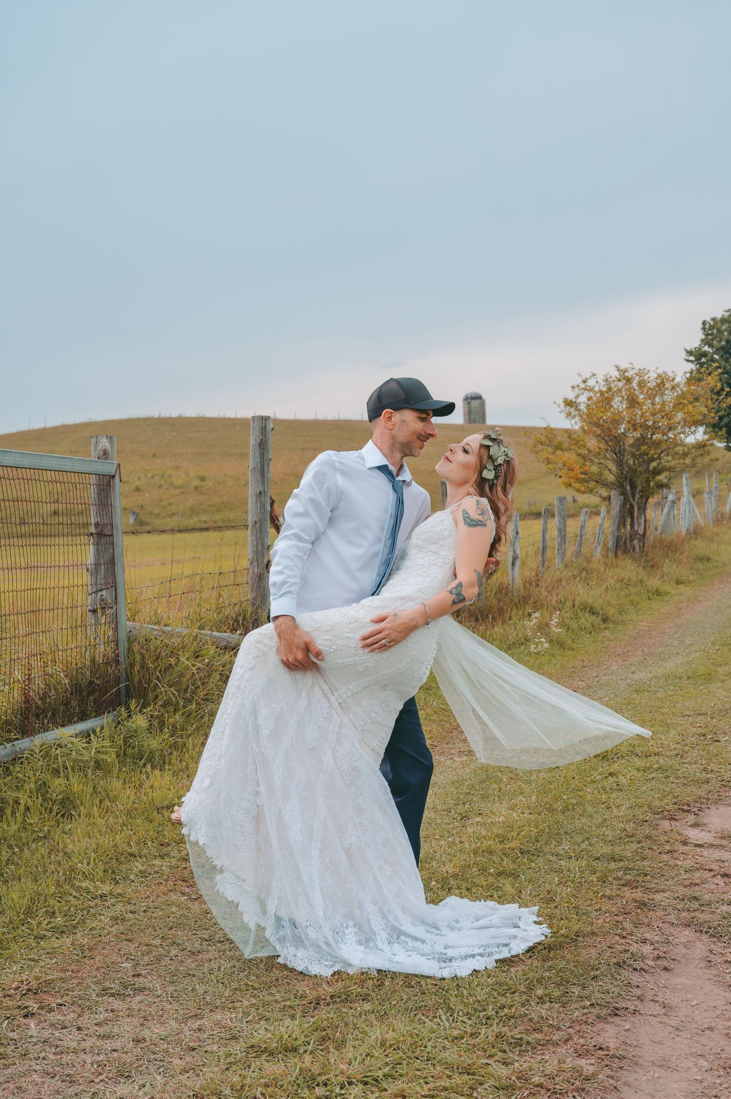 A romantic wedding couple pose on a countryside path with rolling hills in the background.