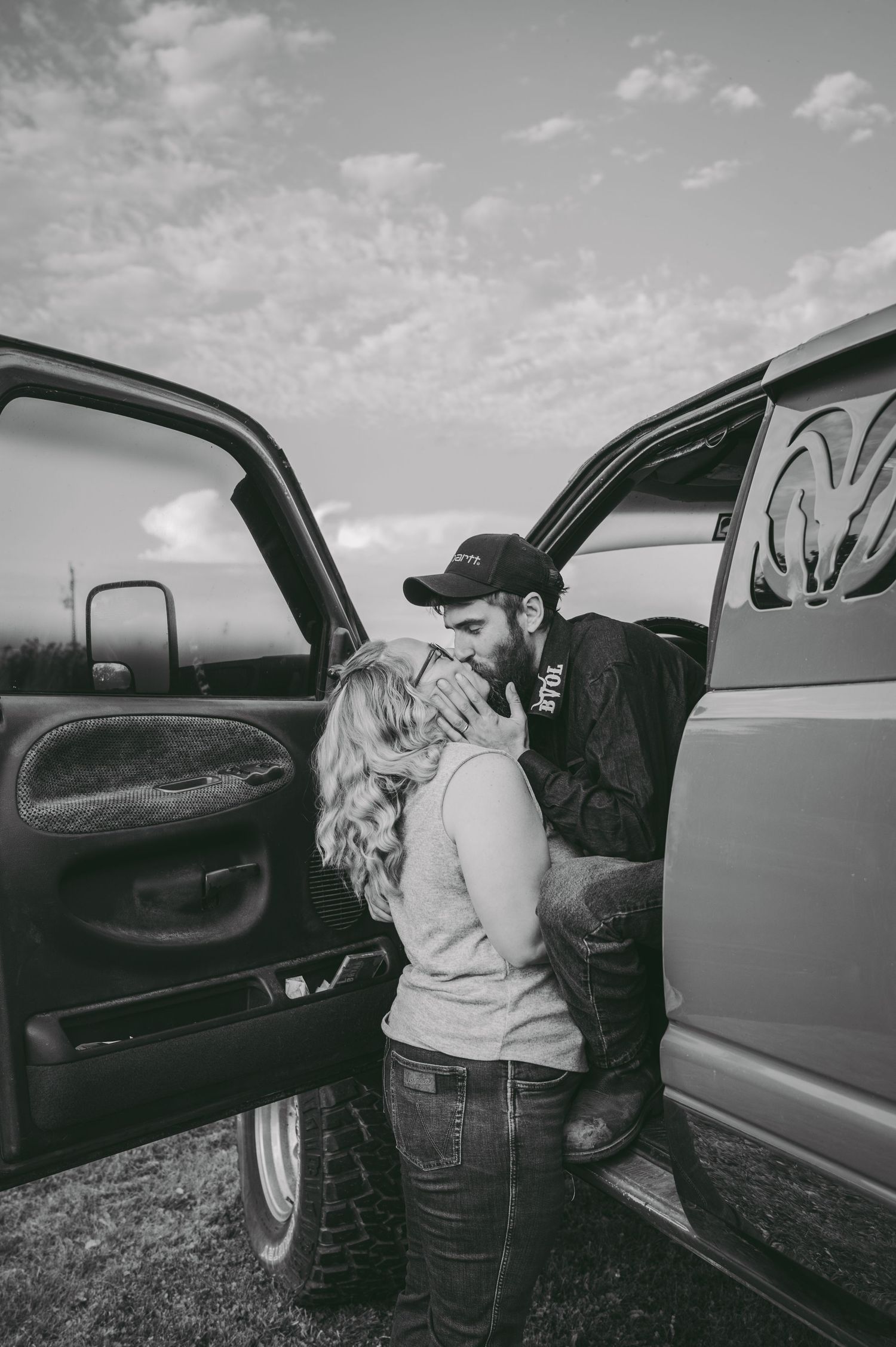 A couple shares a tender moment by a truck door in black and white photography.
