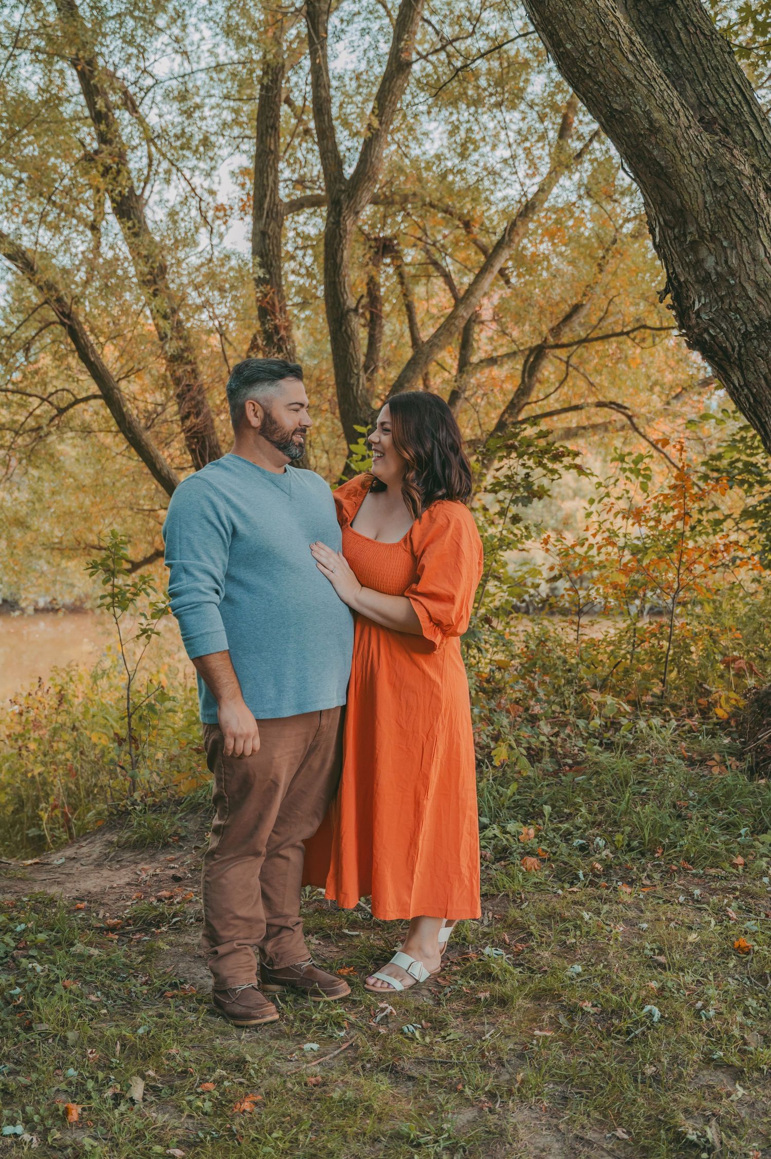 A couple in coordinating blue and orange outfits poses in an autumn setting.